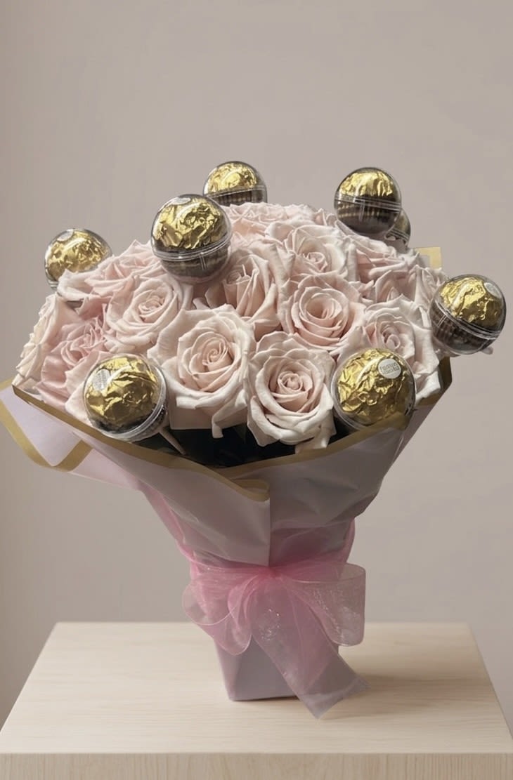 Ferrero Rocher Mother's Day Pink rose Bouquet - A breathtaking and luxurious bouquet featuring Two Dozen premium Blush Pink Roses. The soft petals are elegantly interspersed with gold-wrapped Ferrero Rocher truffles, each protected in a clear decorative sphere. Wrapped in sophisticated white and gold-trimmed paper and finished with a delicate pink organza bow, this bouquet is the ultimate Mother's Day Gift for Mom.