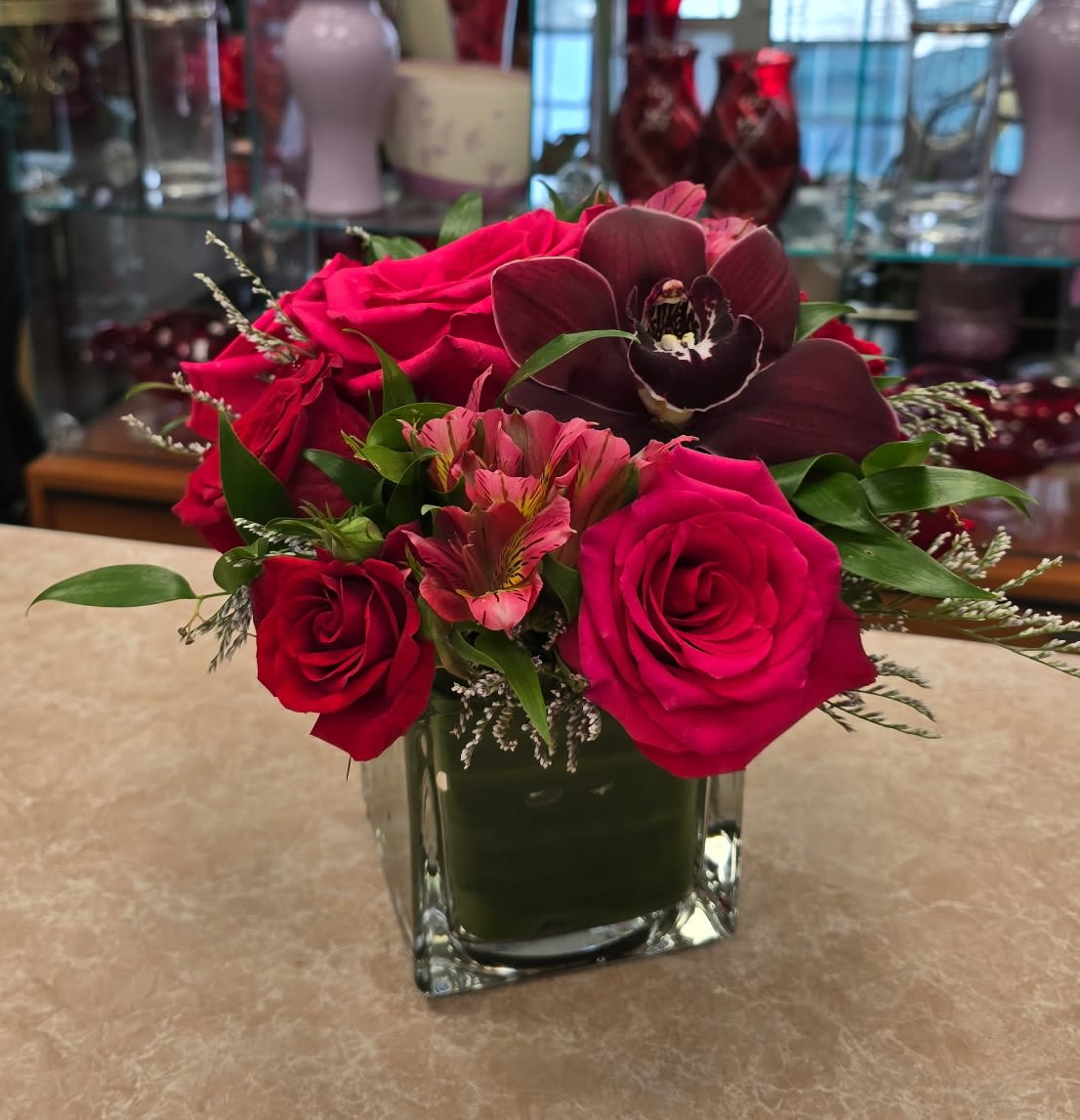 Pink and red roses with a dark orchid in a square glass vase
