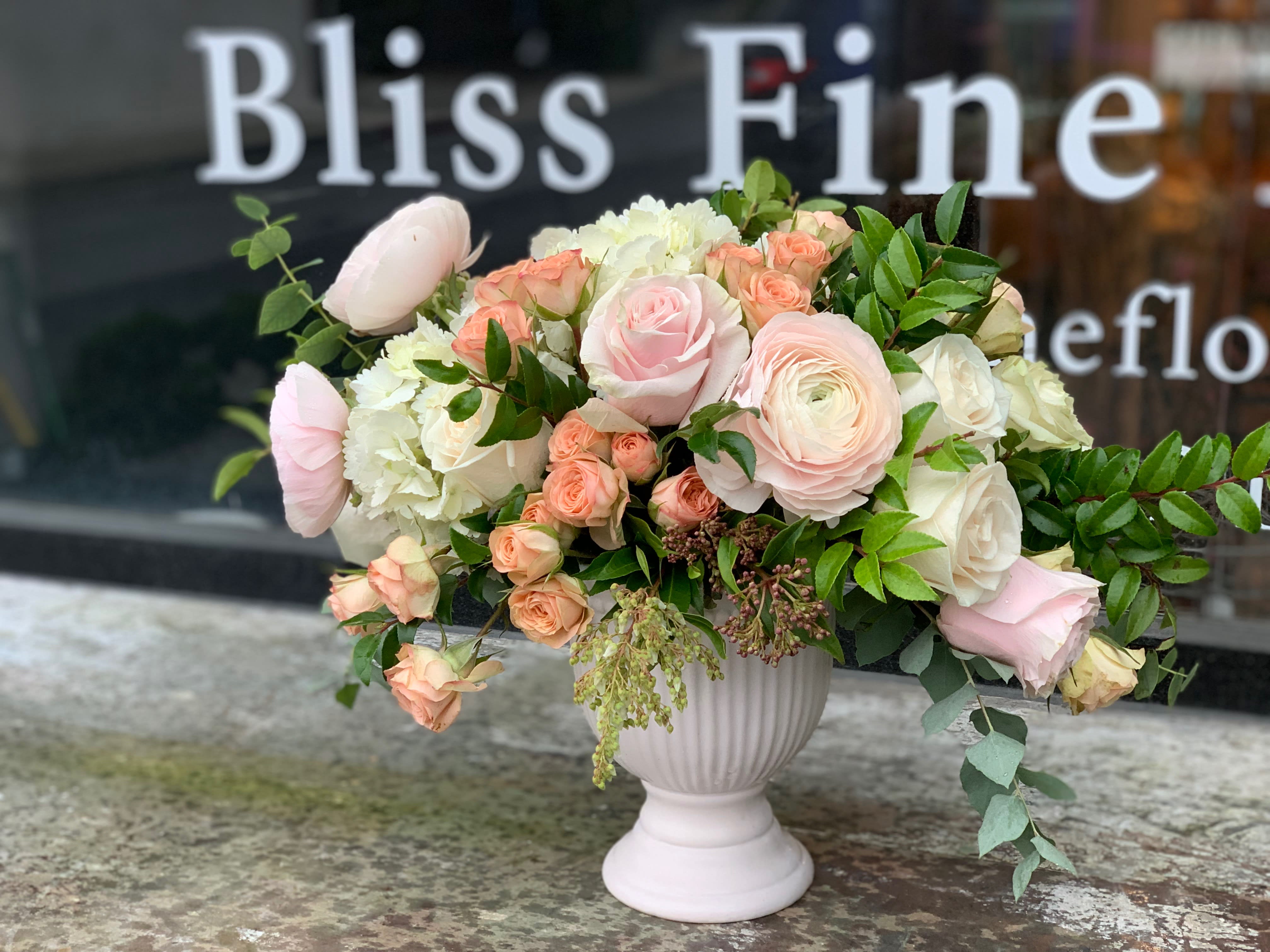 Blush and cream floral arrangement in a white pedestal vase