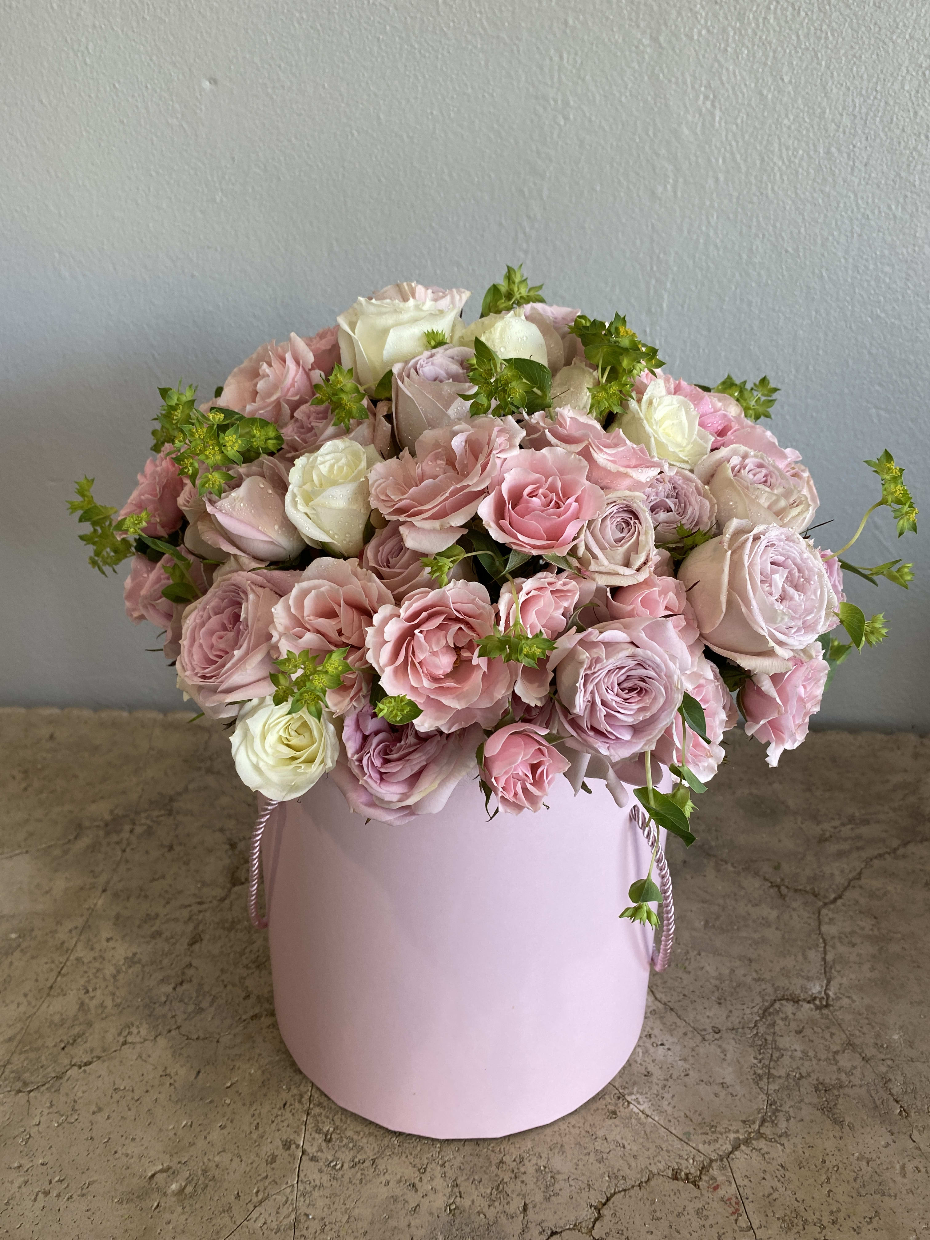 Pink and white roses arranged in a round pastel pink box