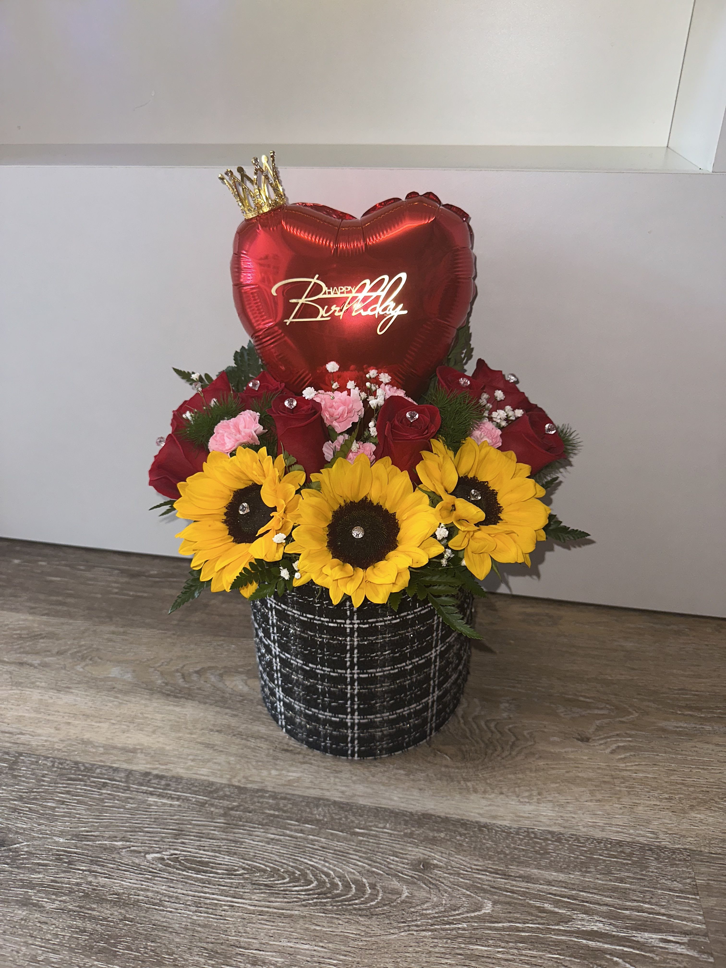 Birthday flower arrangement with sunflowers, red roses, and a heart balloon in a black container