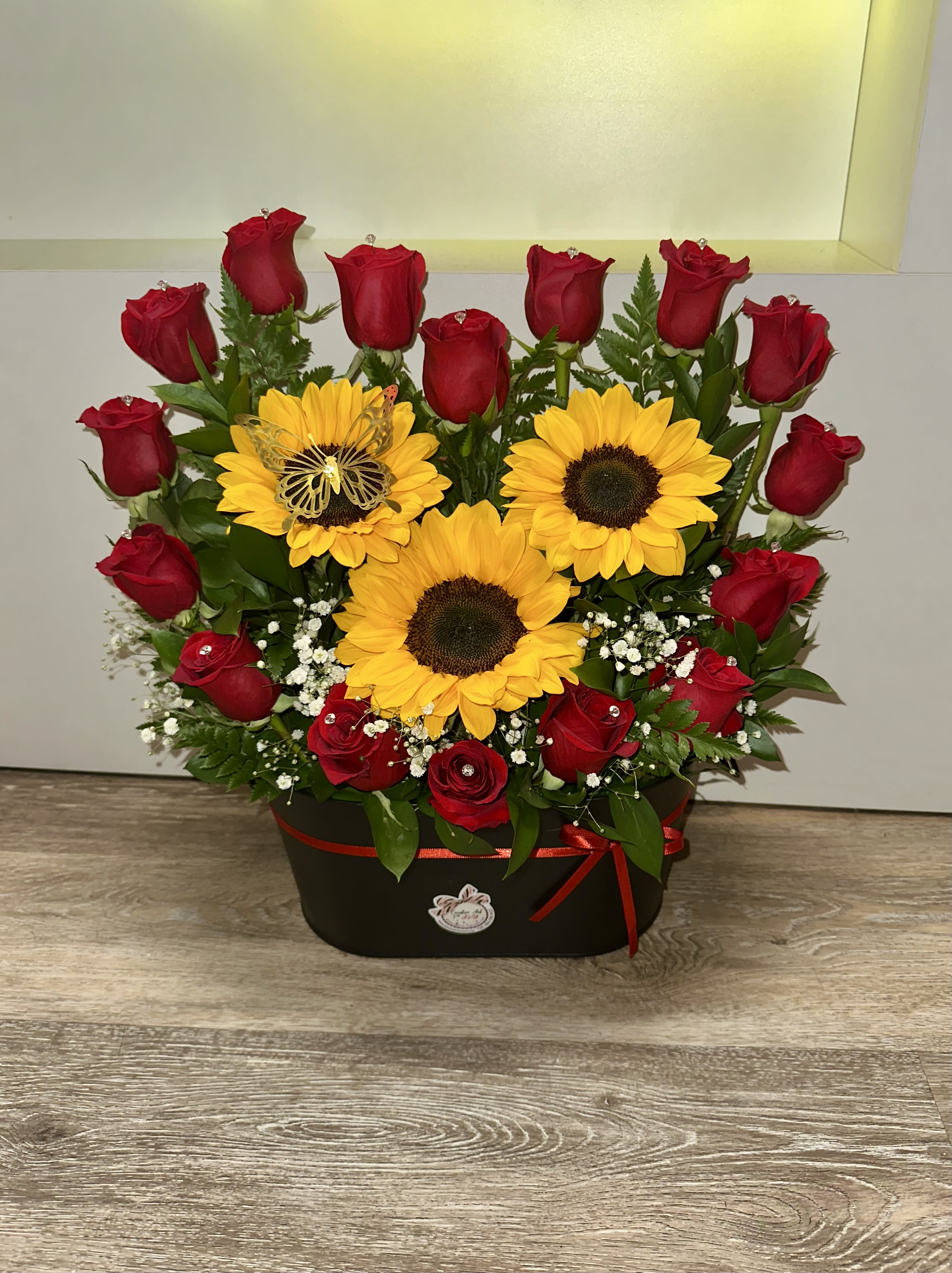 Red roses and yellow sunflowers arranged in a black box with a red ribbon.