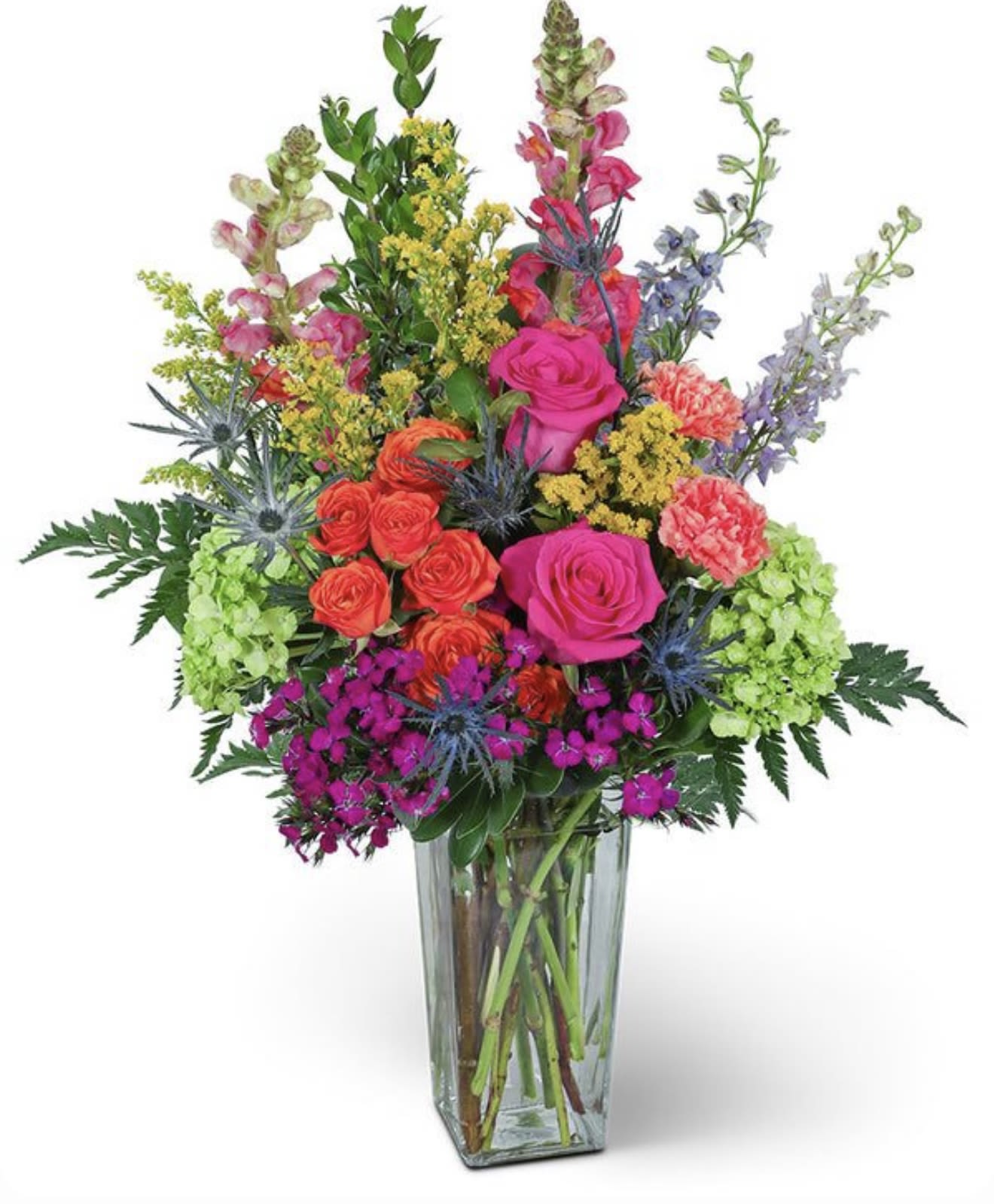 Sweet sunrise - Bright, garden-fresh color greets the eye in this Sweet sunrise flower arrangement - a lively mixed bouquet perfect for a birthday, congratulations, or a cheerful just‑because gift. The upright, celebratory profile and bold palette of pinks, reds, yellows and purples read as joyful and abundant, so the person you're thinking of will feel seen and celebrated the moment it arrives.  This arrangement layers bright pink and red roses with coral carnations, tall snapdragon spikes and blue delphinium/thistle‑like accents for height and texture. Sunflower and yellow clustered filler blooms plus orange and white daisy‑style flowers and delicate alstroemeria add playful contrast, all presented in a clear glass vase for a clean, modern finish. The mix is dense and garden‑style yet lively and airy in places, creating a festive, energetic display that suits many occasions.  Designed to make someone feel genuinely celebrated, Sweet sunrise works well for birthdays, thank‑yous, congratulations, or to brighten an ordinary day. Vase dimensions and specific stem counts vary by size-choose the size that fits your occasion-and keep flowers fresh with regular water changes and a cool spot away from direct heat.