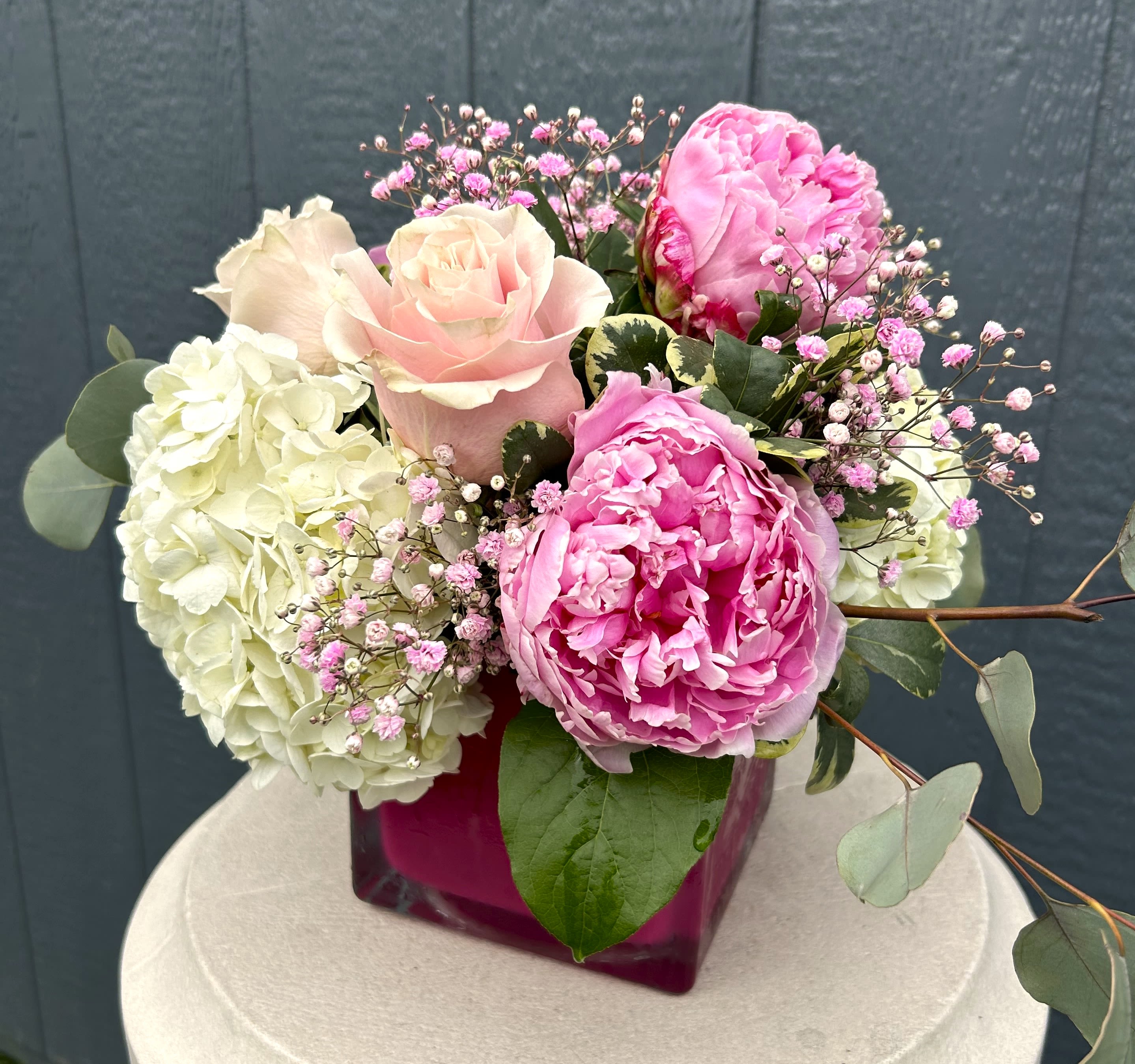 Pink roses and peonies arranged with white hydrangeas in a magenta vase