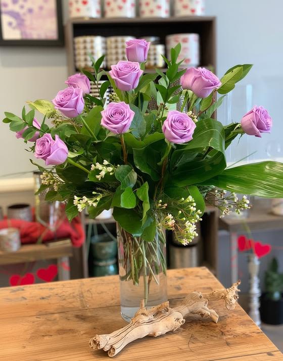 Lavender roses arranged in a clear glass vase with greenery