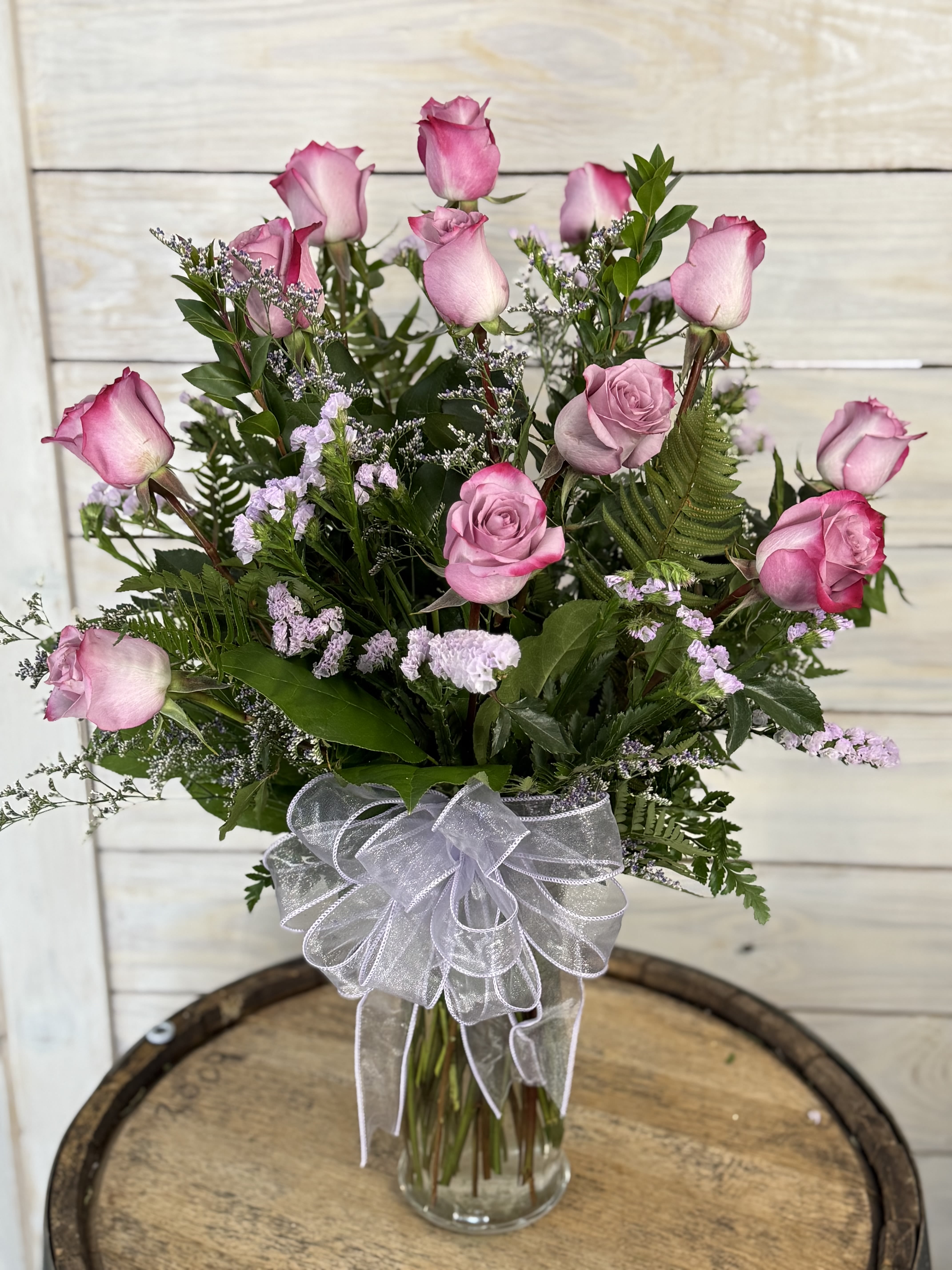 Pink roses arranged in a clear glass vase with a white ribbon bow