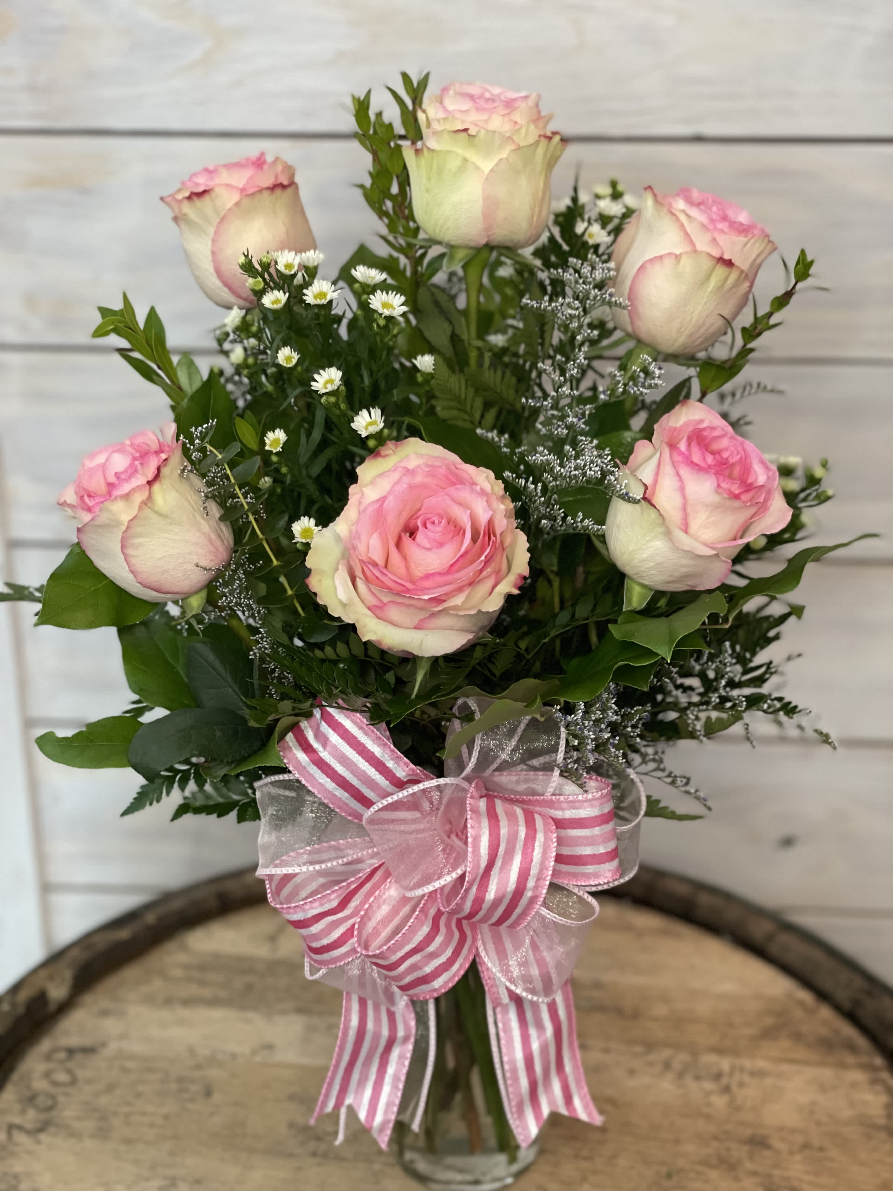 Pink and white roses arranged in a glass vase with a striped ribbon