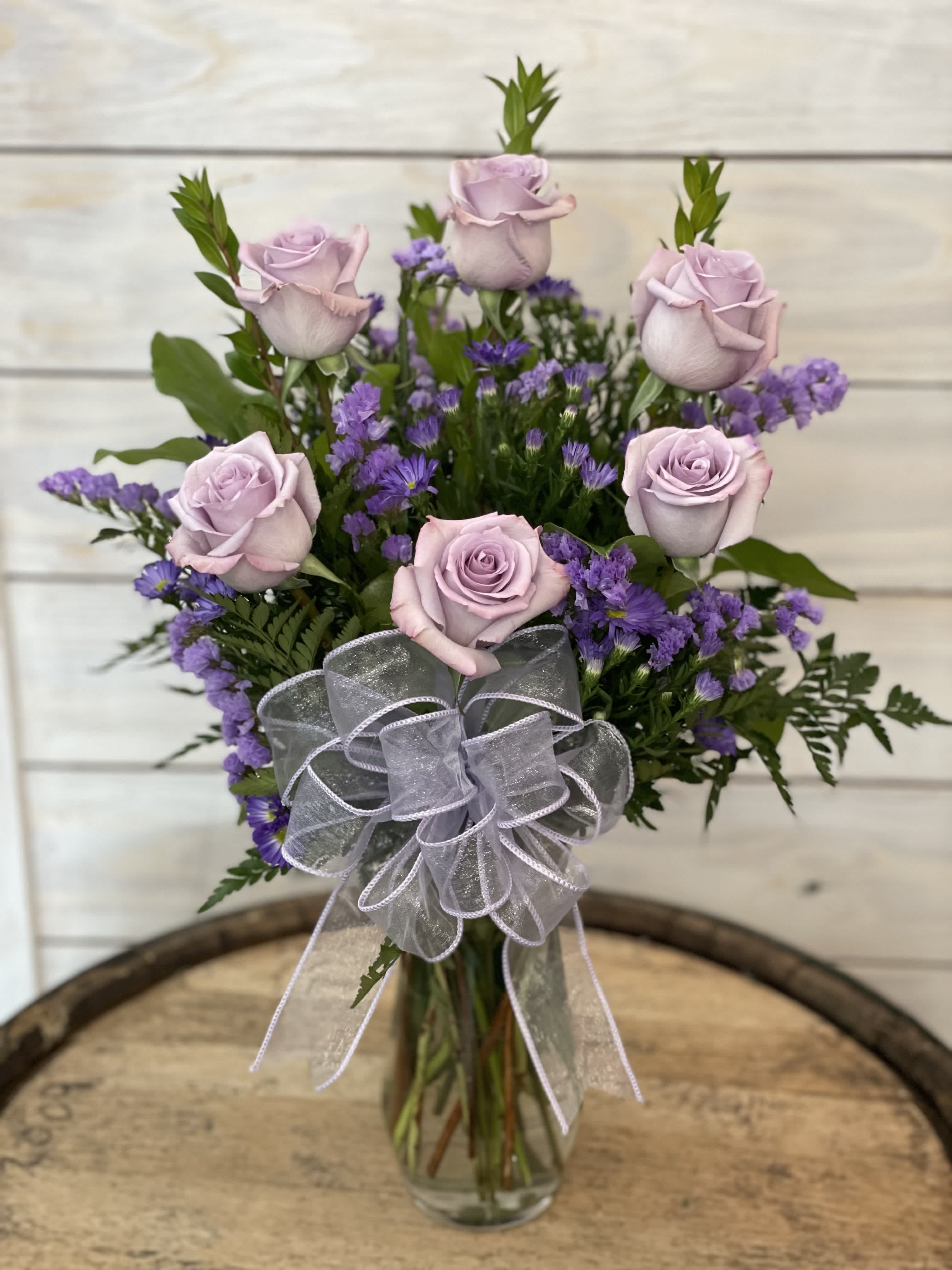 Lavender roses and purple filler flowers in a clear glass vase with a sheer bow