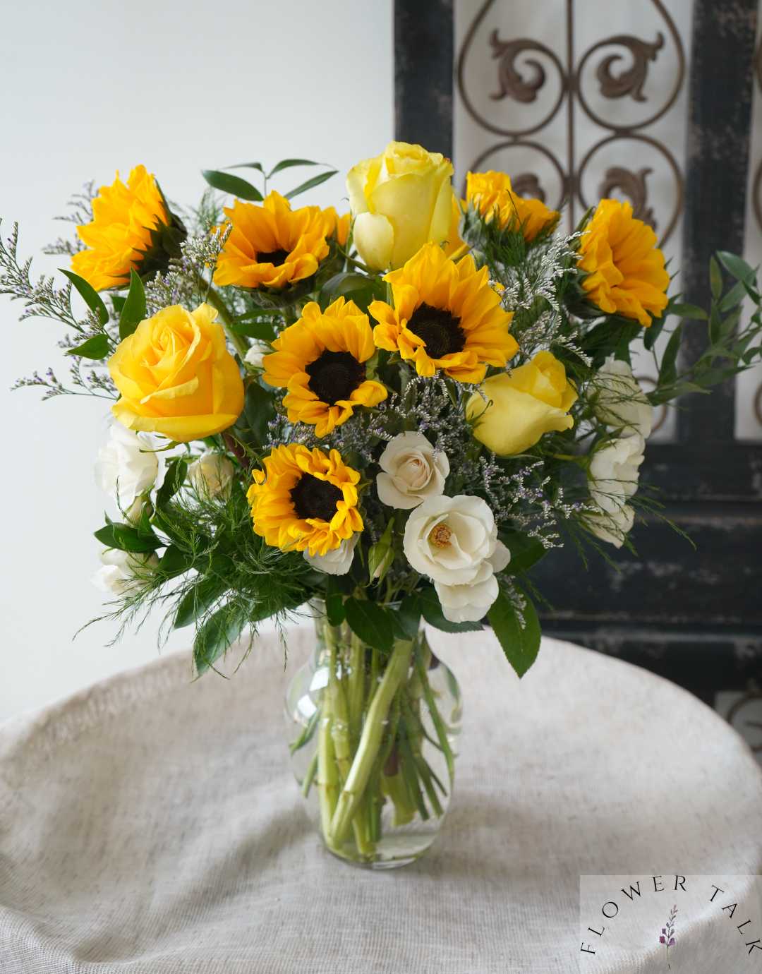 Yellow roses and sunflowers arranged in a clear glass vase