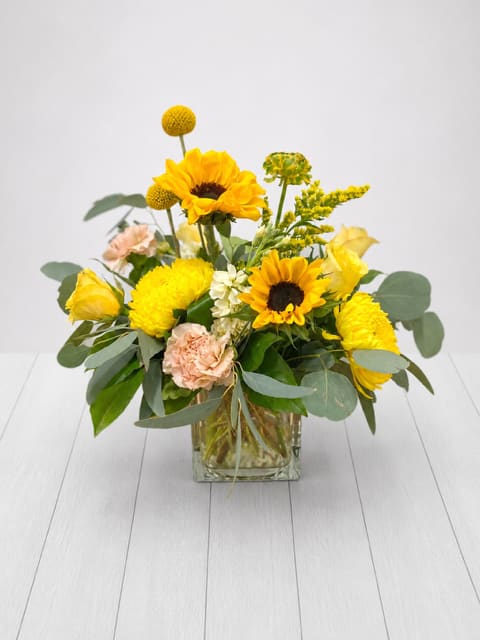 Sunny Side - Sunny Side Yellow and Sunflower Floral Arrangement in Glass Vase  Sunny Side is a bright, cheerful yellow and sunflower floral arrangement in a clear glass vase, hand designed by a local East Moline florist with delivery available.  Sunny Side features a fresh, balanced design with golden sunflowers, yellow blooms, and soft complementary accents, arranged in a lush, garden inspired style with blooms selected at the designer’s discretion based on seasonal availability.  Sunny Side is available for delivery in East Moline, Moline, Rock Island, Silvis, Davenport, and Bettendorf, offering a naturally radiant option for gifting across the Quad Cities.  Approximately 13” x 13” 