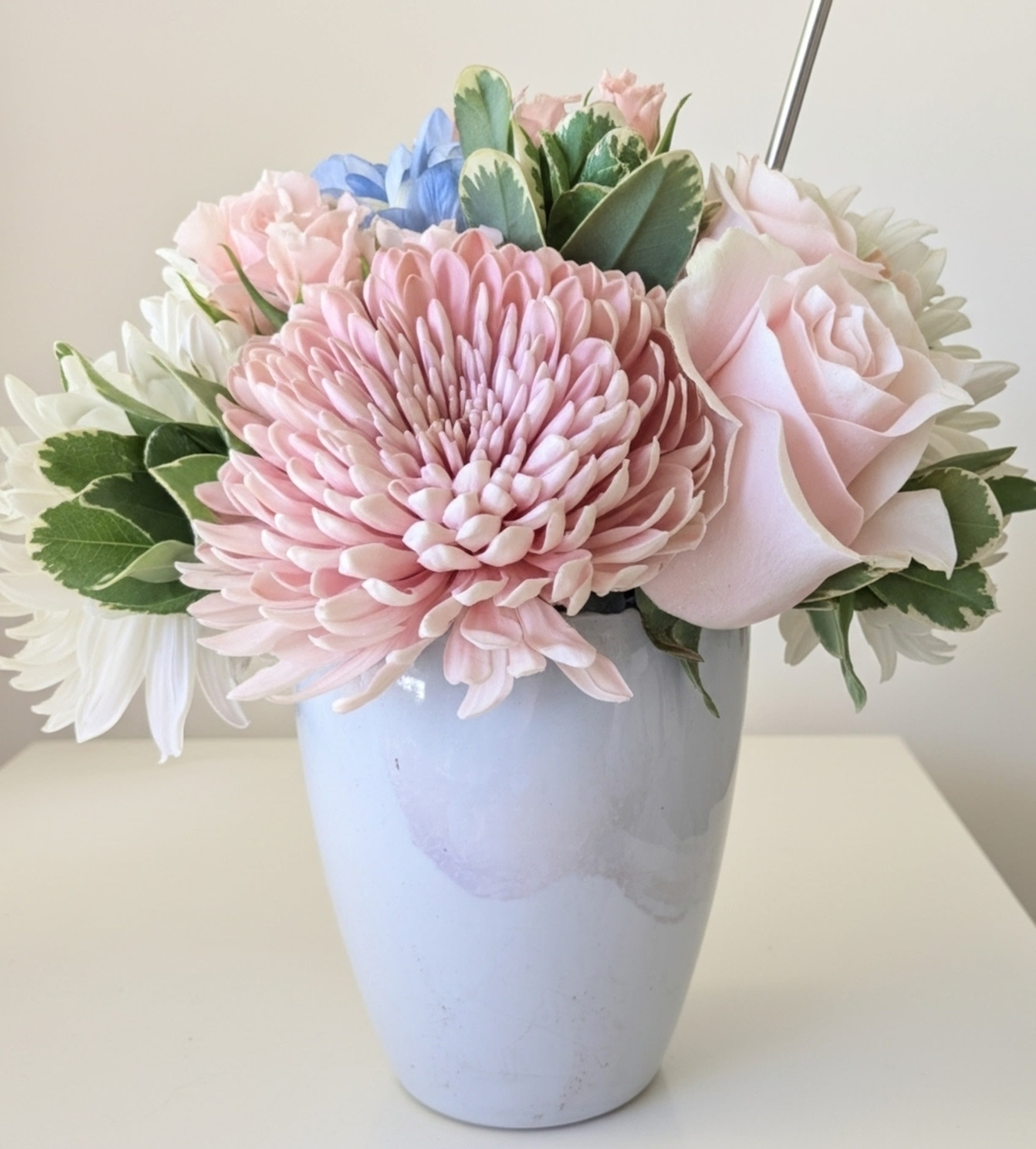 Pastel arrangement of pink chrysanthemum, rose, and white flowers in a light blue vase