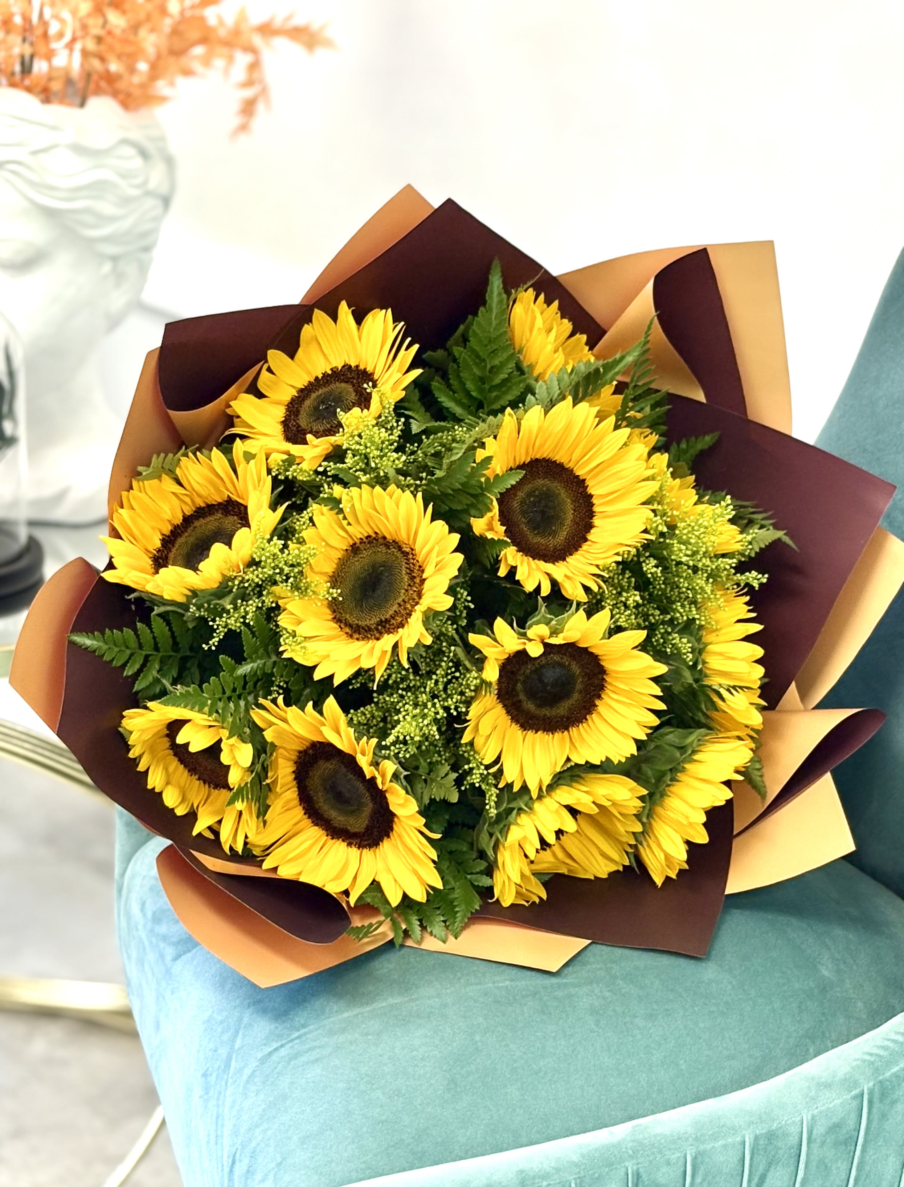 Bouquet of bright yellow sunflowers with greenery wrapped in brown and tan paper on a teal chair