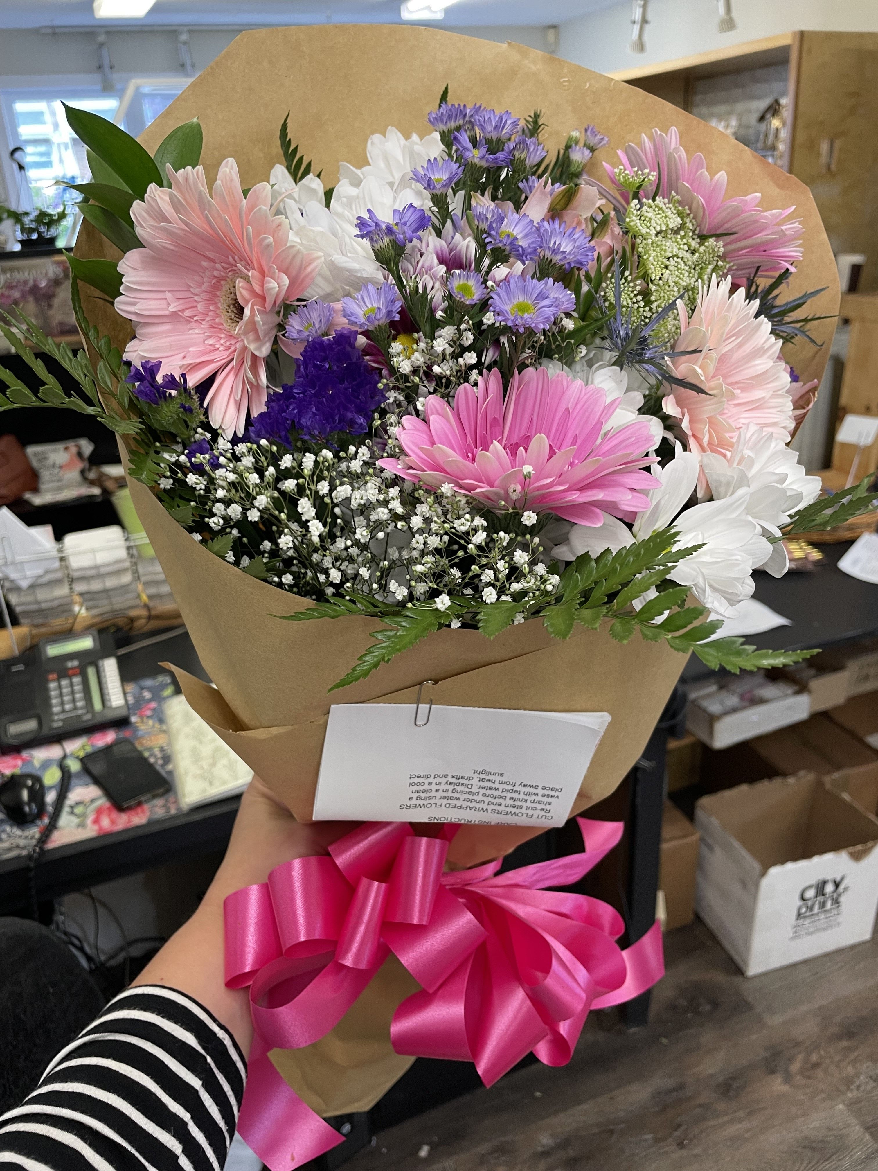 Bouquet of pink, white, and purple daisies wrapped in brown paper with a pink ribbon