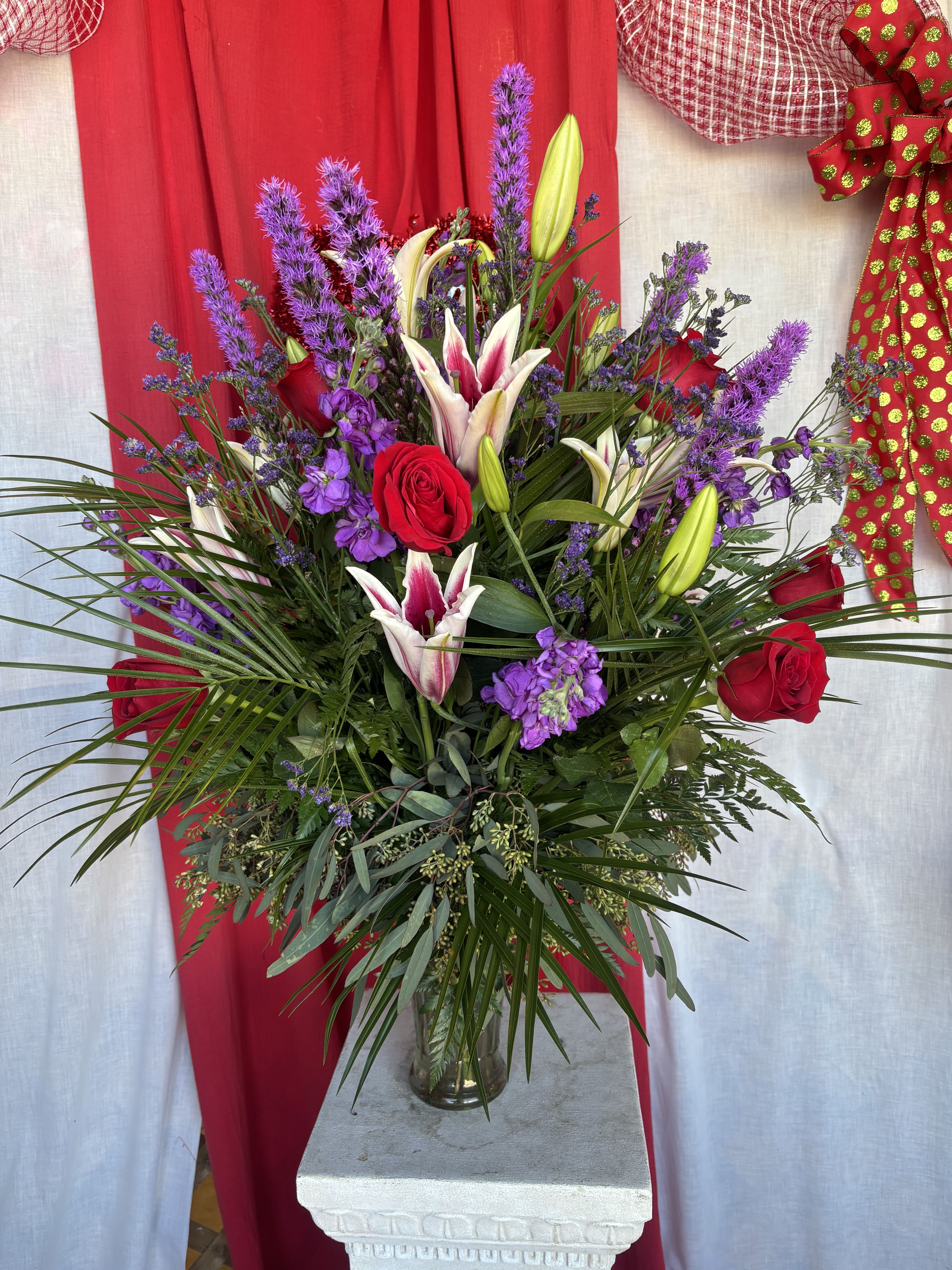 Tall bouquet of red roses, purple flowers, and white lilies in a glass vase