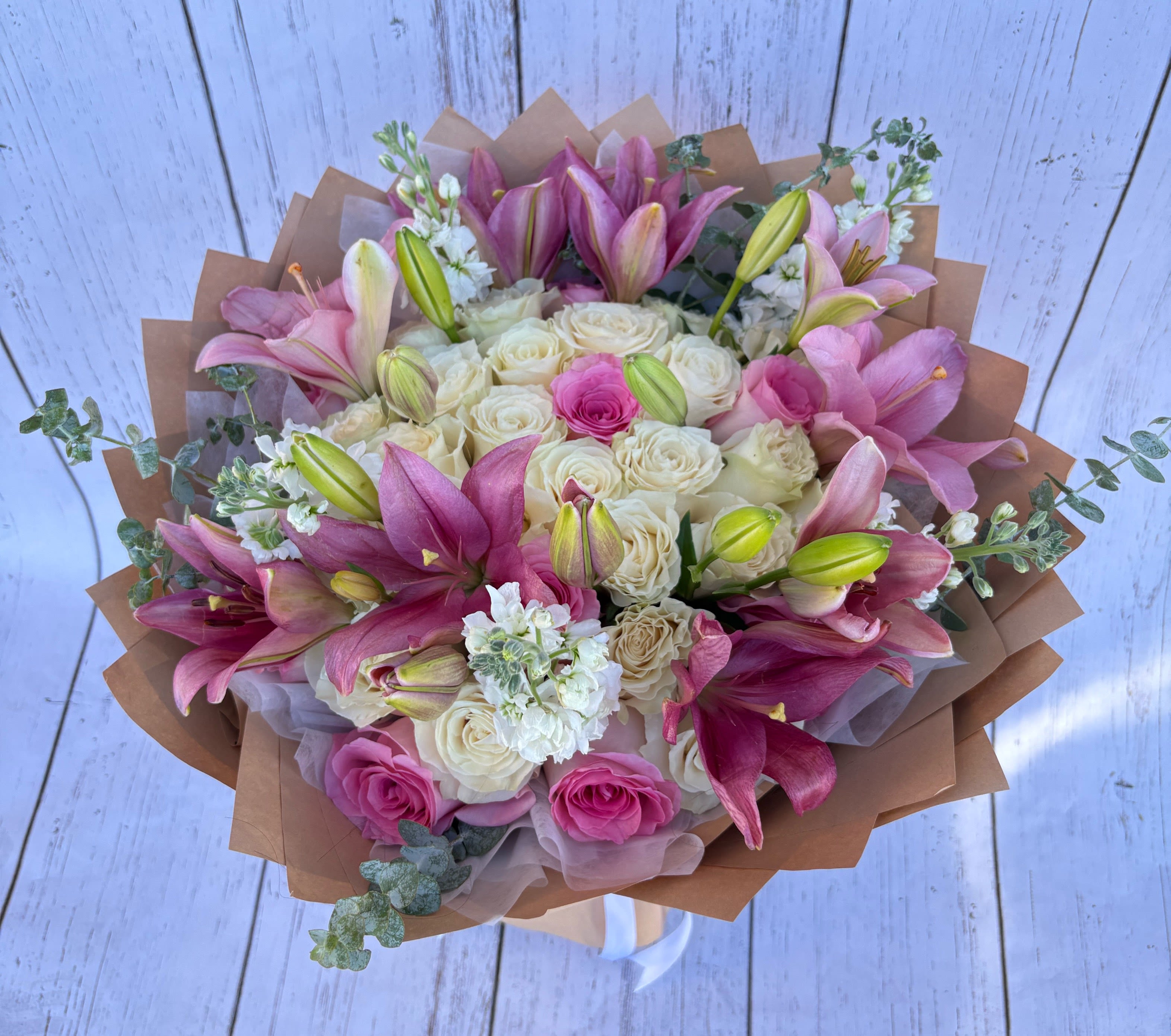 Bouquet of pink lilies and cream roses wrapped in brown paper