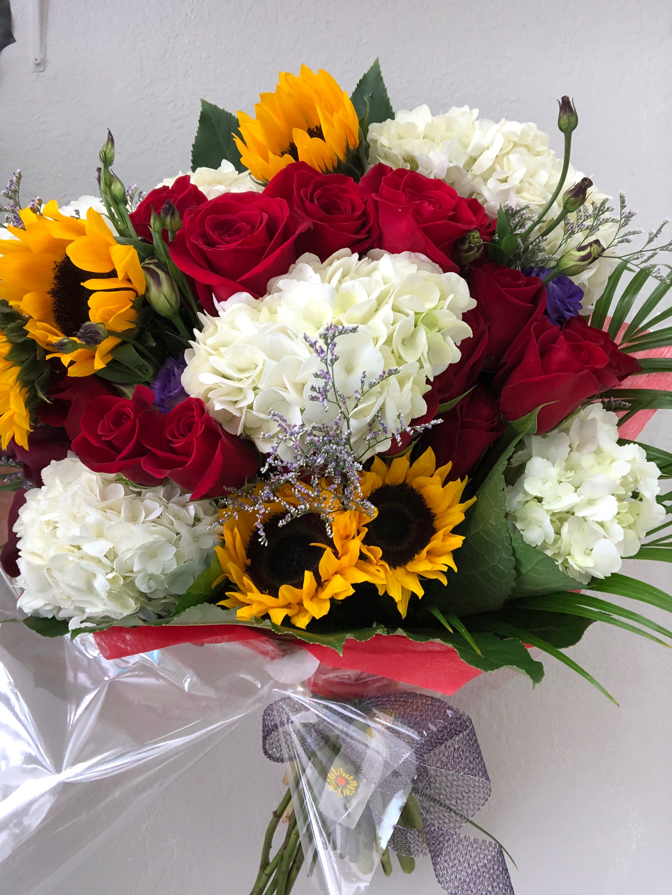Bouquet of red roses, white hydrangeas, and sunflowers wrapped in clear plastic