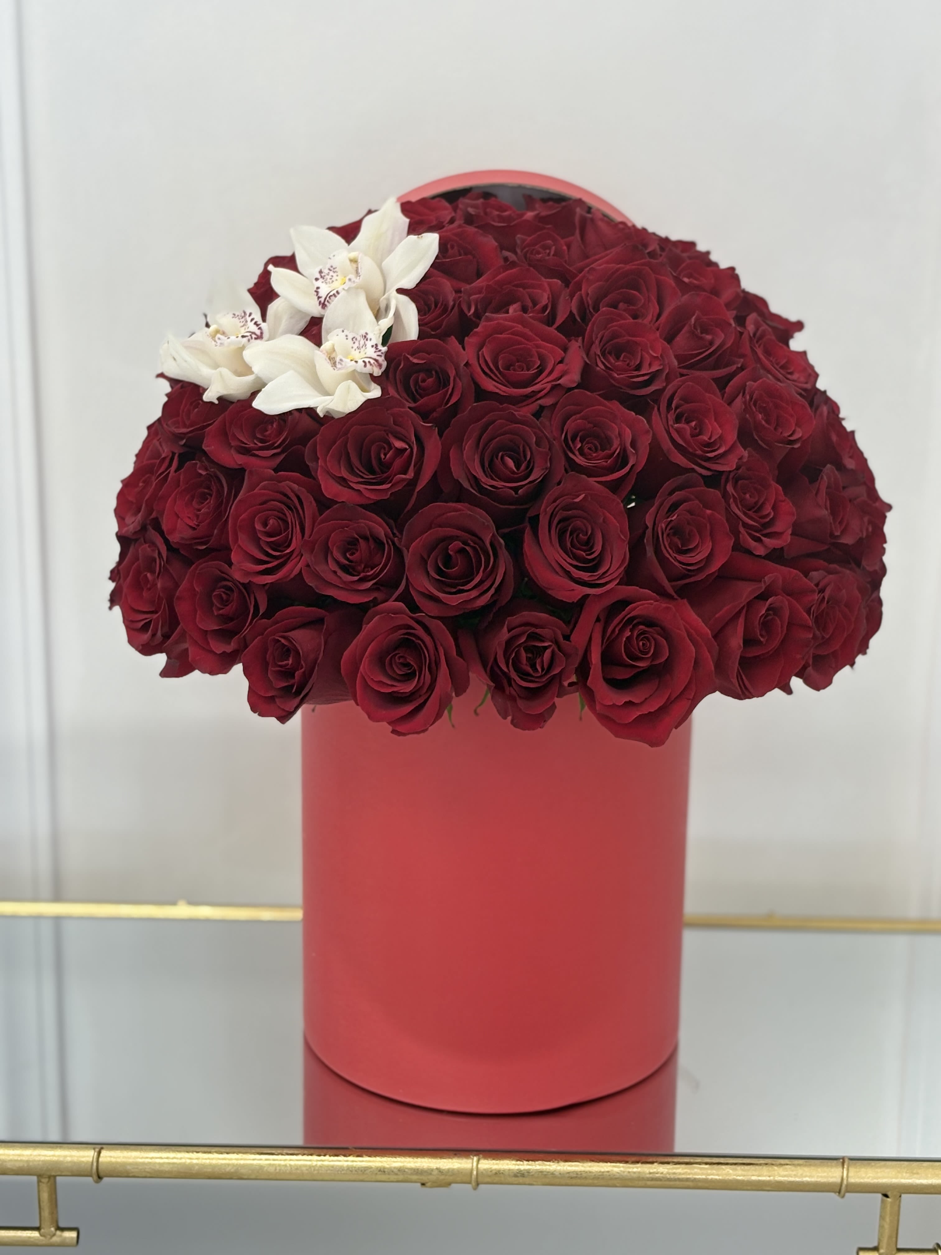 Red rose arrangement in a pink cylindrical box with white orchids