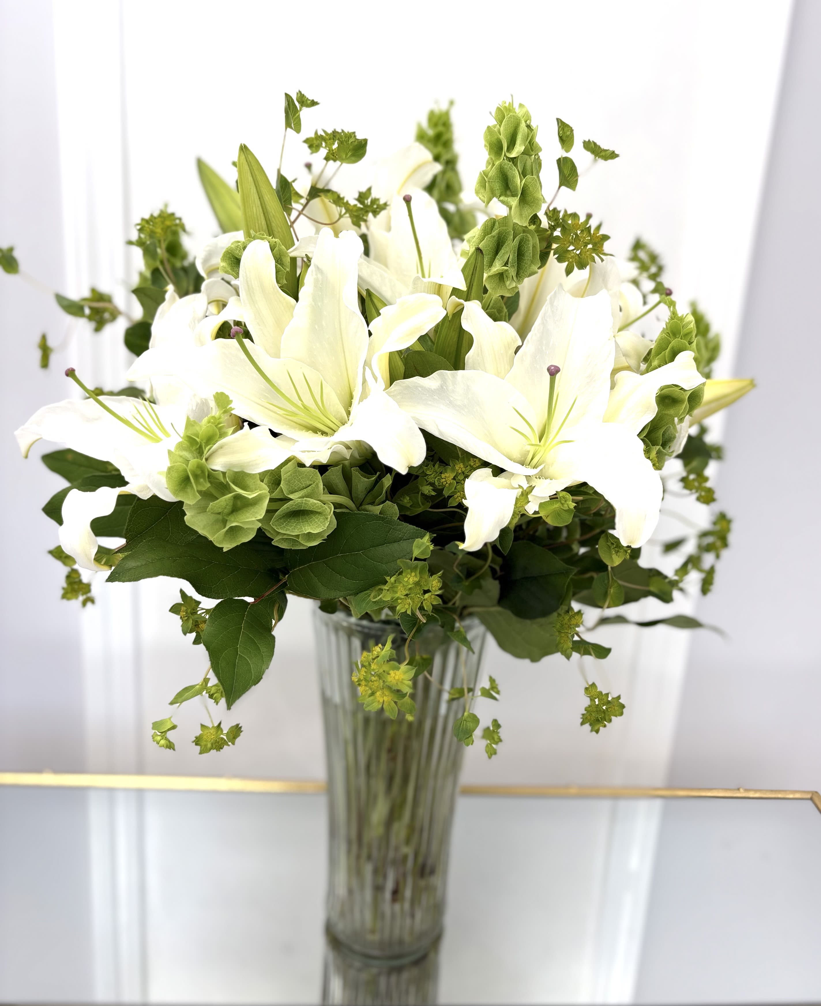 White lilies in a clear glass vase with green filler flowers