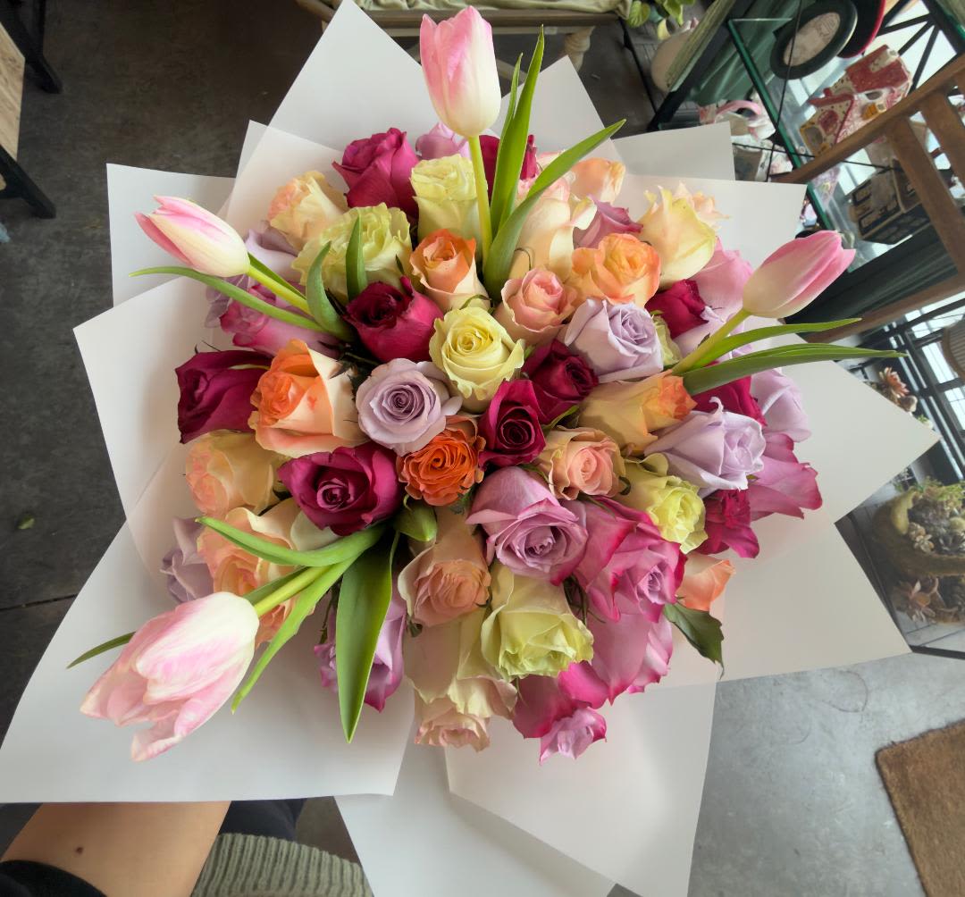 Bouquet of multicolored roses with pink tulips wrapped in white paper