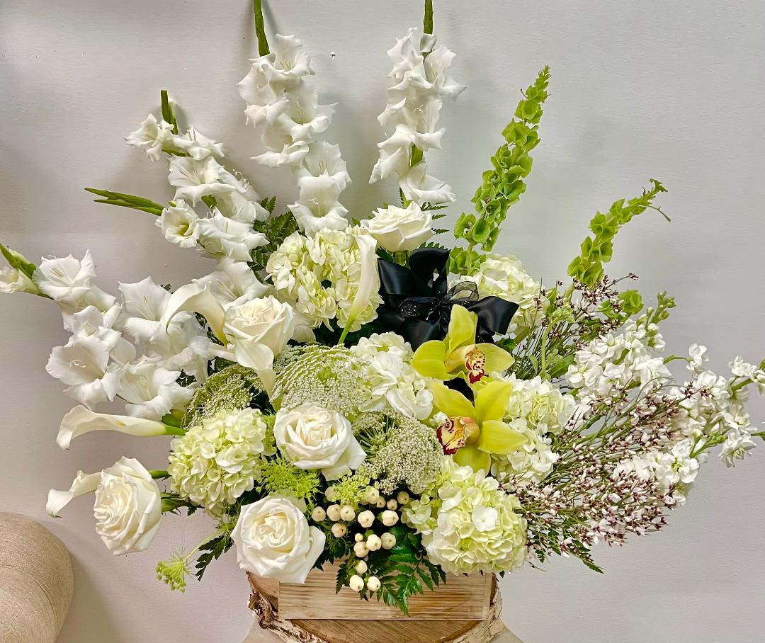 White floral arrangement with roses, orchids, and tall gladiolus in a wooden box