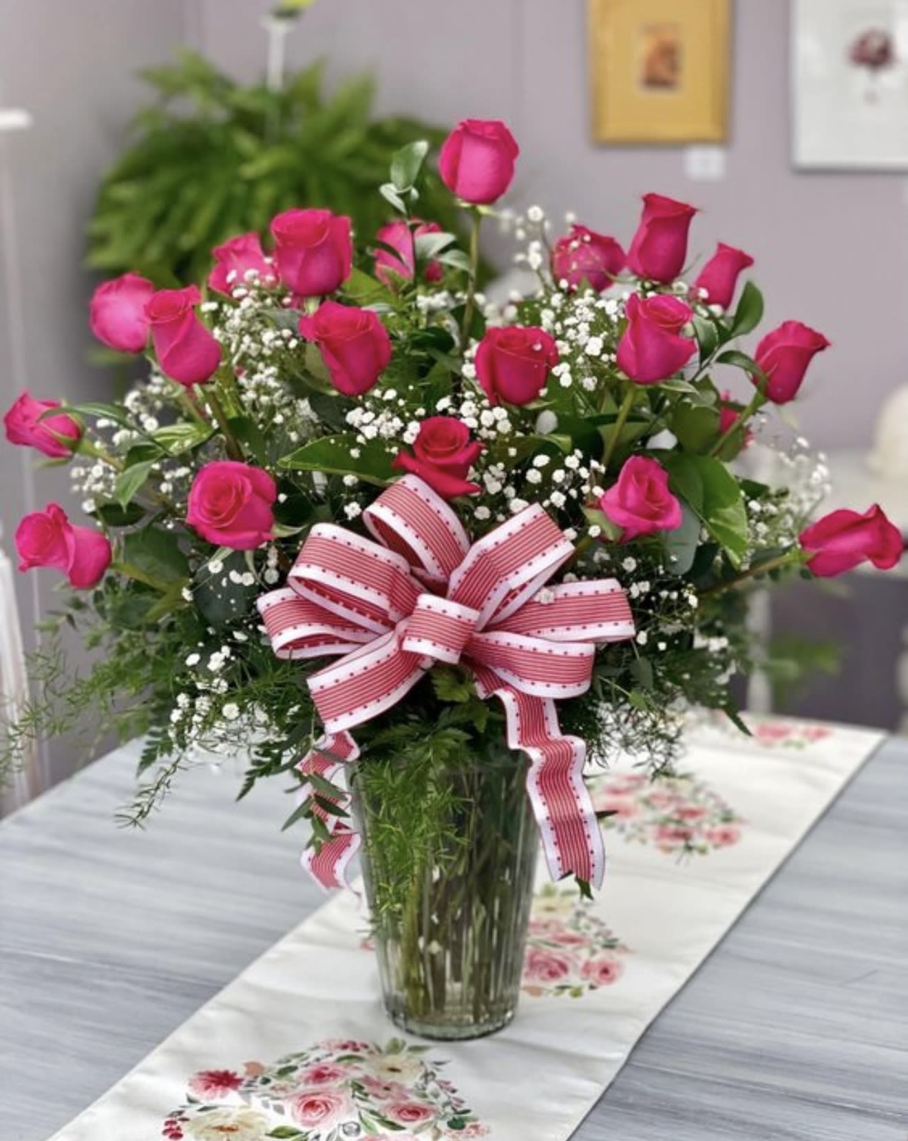 Sweet mother  - A lush cluster of hot pink roses takes center stage in this flower arrangement, a sweet mother gift that reads as bright, romantic, and distinctly feminine - perfect for Mother's Day, a birthday, anniversary, or simply to say "I'm thinking of you." The upright, full composition and celebratory pink-and-white striped ribbon make the recipient feel cherished and seen the moment the vase is set down.  This bouquet pairs vivid hot pink roses with small white filler flowers and airy green foliage for contrast, arranged in a clear glass vase with a large decorative bow tied at the front. The overall look is classic and gift-ready: compact enough for a table or counter yet full enough to make an immediate impact. Simple care-fresh water and a cool spot away from direct sun-keeps the blooms looking their best while they brighten someone's day.