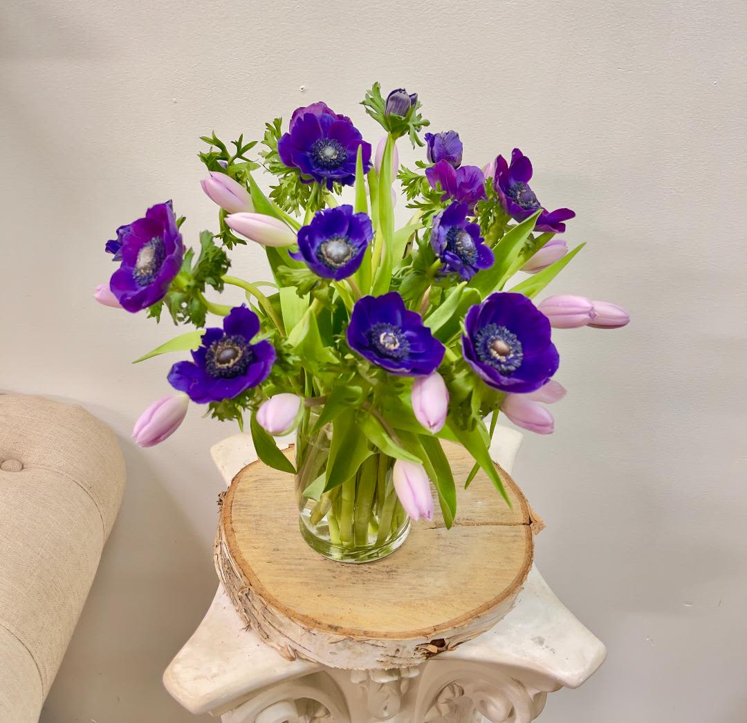 Purple anemones and pale pink tulips in a clear glass vase