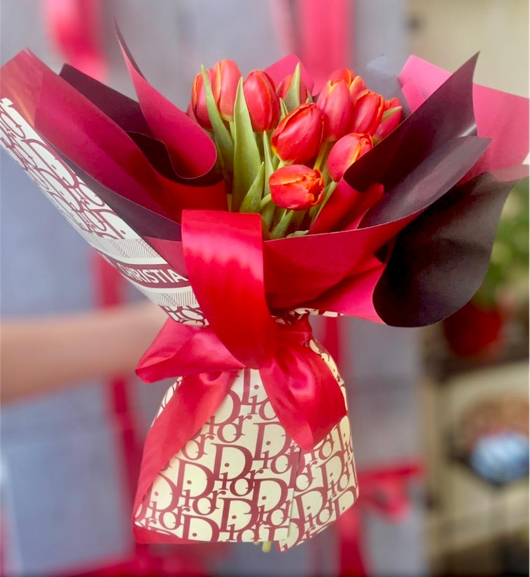 Bouquet of red tulips wrapped in pink and burgundy paper with a satin ribbon