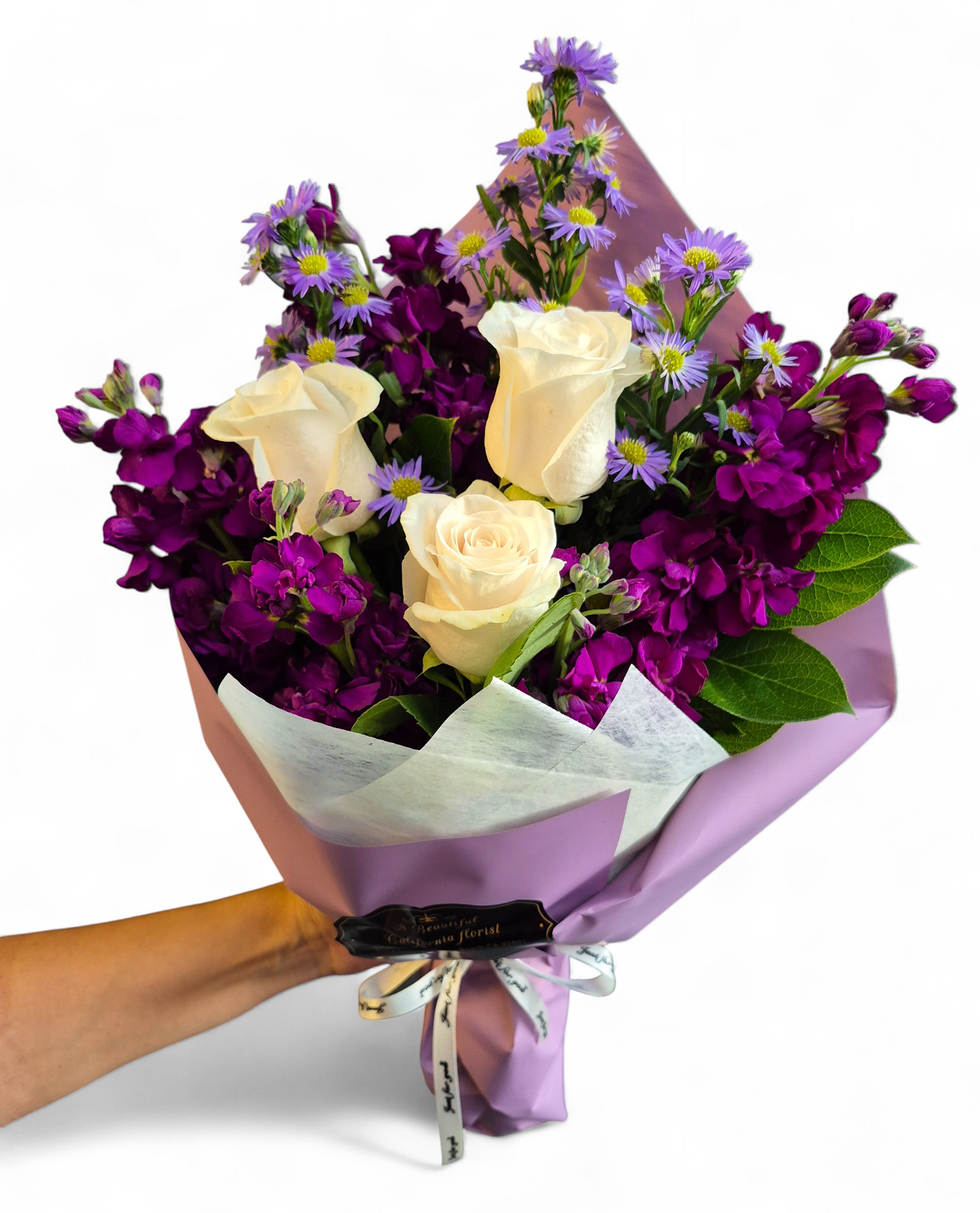 Angelique Enchantment Wrap Bouquet - Indulge in the regal beauty of our Angelique's Enchantment Bouquet, a stunning hand-tied floral arrangement featuring a captivating contrast of colors. This popular design showcases luxurious white roses, symbolizing purity and innocence, nestled among deep, fragrant purple stock flowers and delicate lavender asters. The rich, jewel-toned palette is exquisitely wrapped in coordinating tissue and satin paper, creating a truly elegant flower gift.  Perfect for anniversaries, birthdays, expressing admiration, or simply brightening someone's day, this bouquet is a timeless choice.  Order this signature design from A Beautiful California Florist, your well-reviewed and trusted Long Beach flower shop. We are committed to fast service and offer same-day flower delivery across Long Beach and surrounding areas, ensuring your beautiful purple and white flower bouquet arrives fresh and on time.  Key Blooms: White Roses, Purple Stock Flowers, Lavender Asters/Daisies.  Style: Hand-Tied Bouquet, Luxury Floral Wrap.  Perfect For: Anniversary, Valentine's Day, Birthday, Sympathy, Admiration.  Delivery: Same-Day Flower Delivery Long Beach CA is available. Or Pick up at 611 E Carson Street, Suite B, Long Beach, CA, 90807