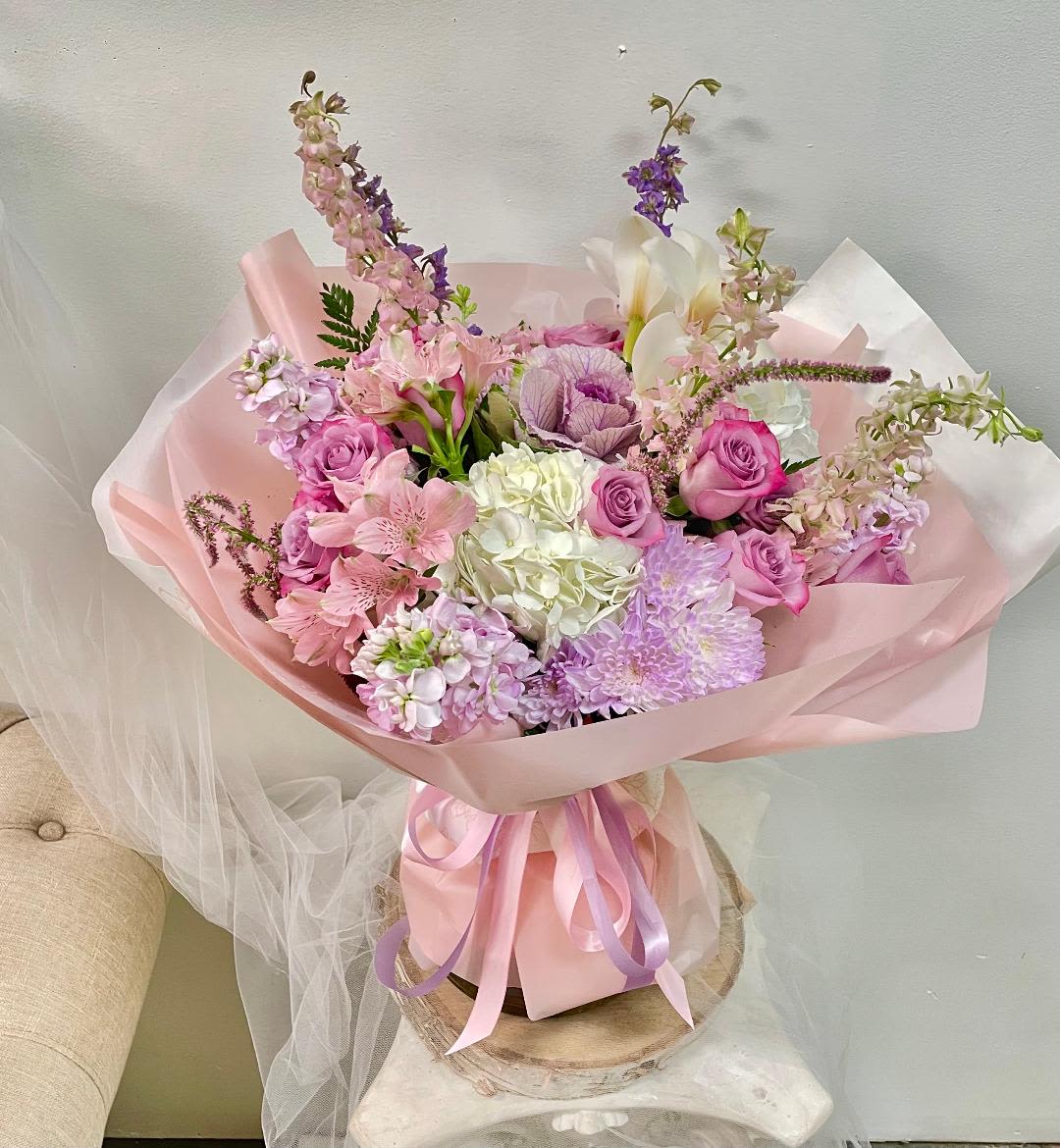 Pink and lavender bouquet with roses, hydrangea, and lilies wrapped in pastel paper