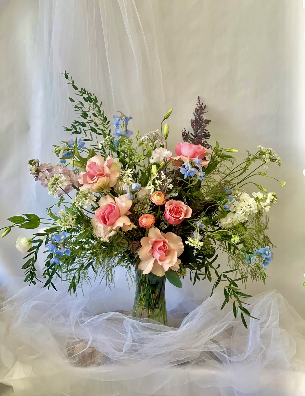 Tall mixed bouquet of pink roses and blue flowers in a glass vase