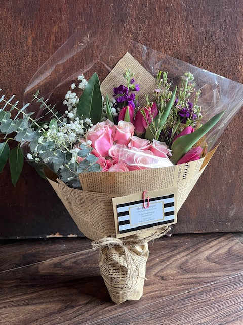 Bouquet of pink roses and purple flowers wrapped in newspaper-style paper