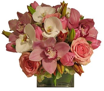 Compact arrangement of pink roses and pink and white orchids in a clear glass cube vase