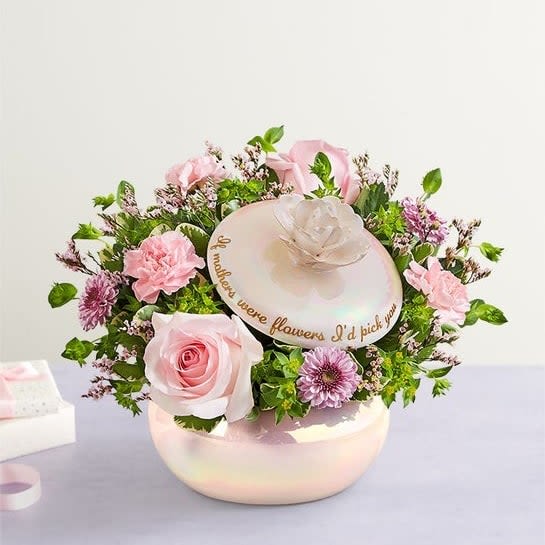 A Mother's Love Pearlized Canister - A Mother's love is forever. This sentiment is beautifully captured in our garden-inspired bouquet, featuring a mix of pastel blooms in our keepsake canister. With an iridescent finish, elegant rosebud lid and heartfelt message, this timeless gift is a lasting reminder of the special bond you share. All-around arrangement with light pink roses and mini carnations, pink Limonium and lavender button poms; accented with assorted greenery   Artistically designed in our exclusive container, designed in an iridescent finish on a ceramic base, embellished with a budding rose and finished with a gold foil sentiment, “If mothers were flowers I’d pick you."  Large arrangement measures approximately 10"H x 10"W Small arrangement measures approximately 9"H x 9"W  