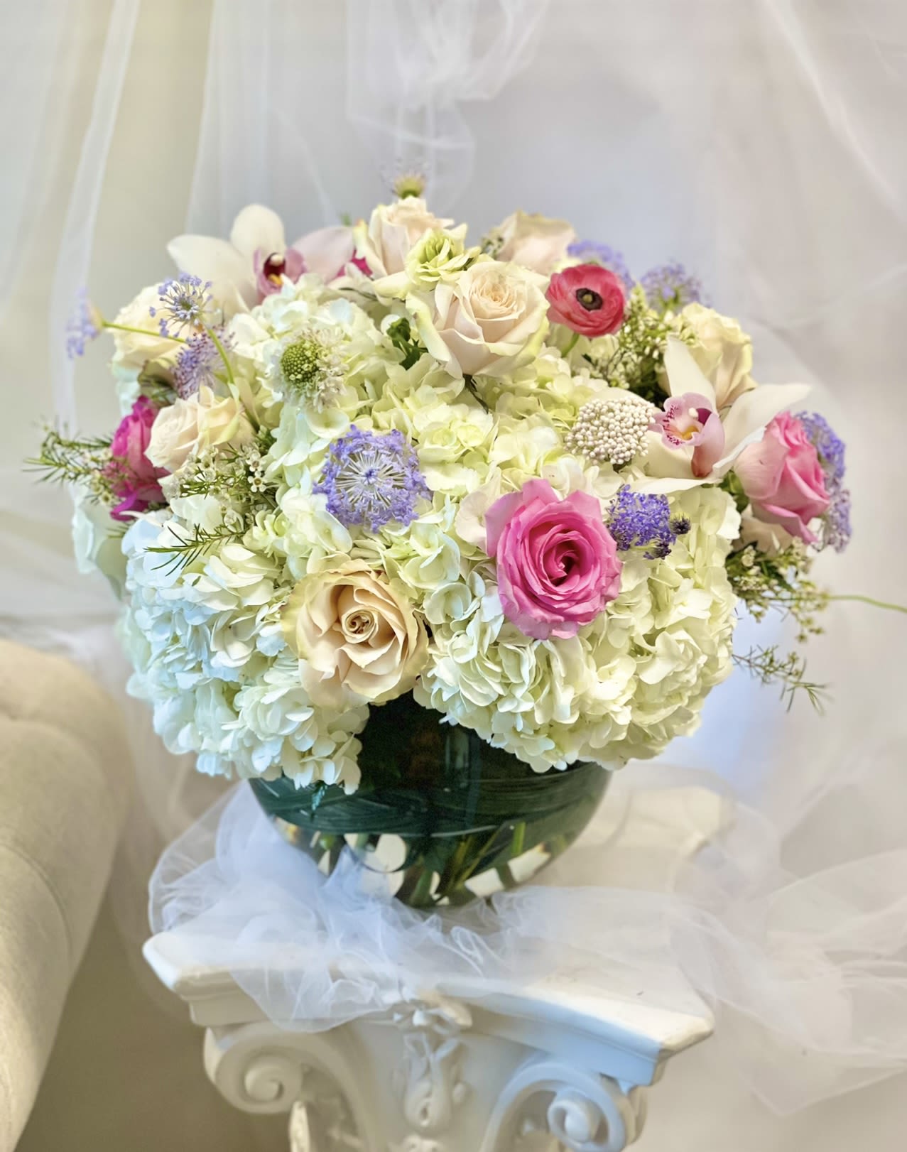 Bouquet of pale hydrangeas, pink roses, and white orchids in a glass vase