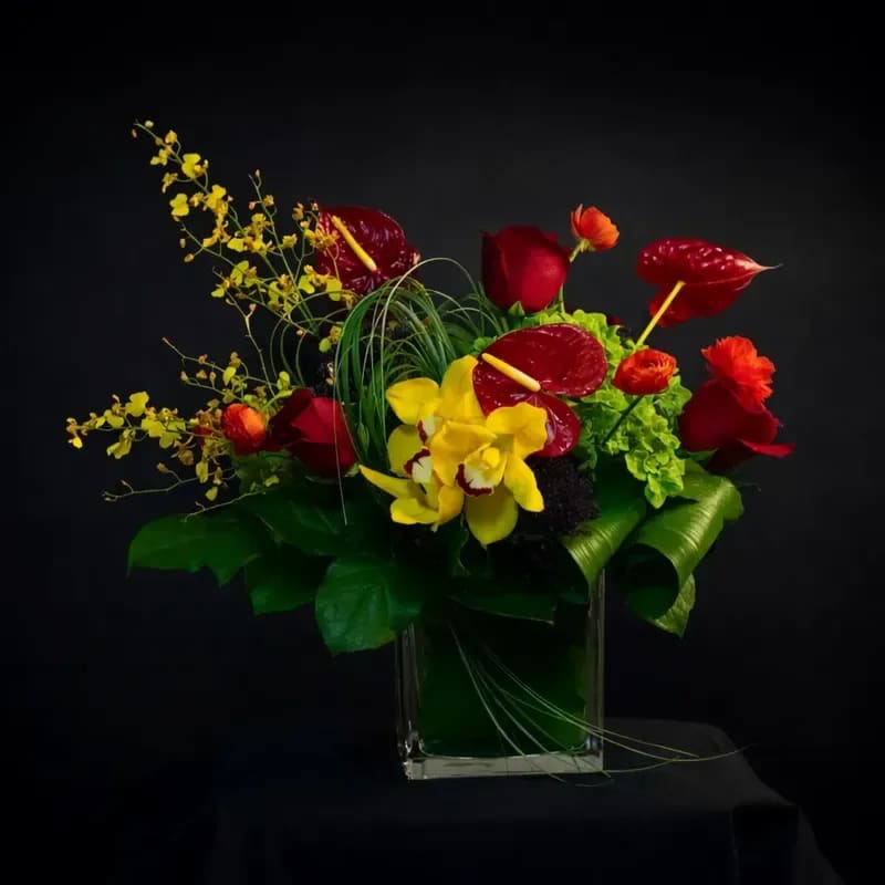 Crimson Desire - A striking expression of passion and elegance, Crimson Desire is designed to captivate. Deep crimson roses and glossy red anthuriums intertwine with radiant golden cymbidium orchids and vibrant ranunculus, creating a bold contrast against rich, sculptural greenery. Dramatic yet refined, this arrangement is a modern statement of love — perfect for those who appreciate romance with intensity and style.