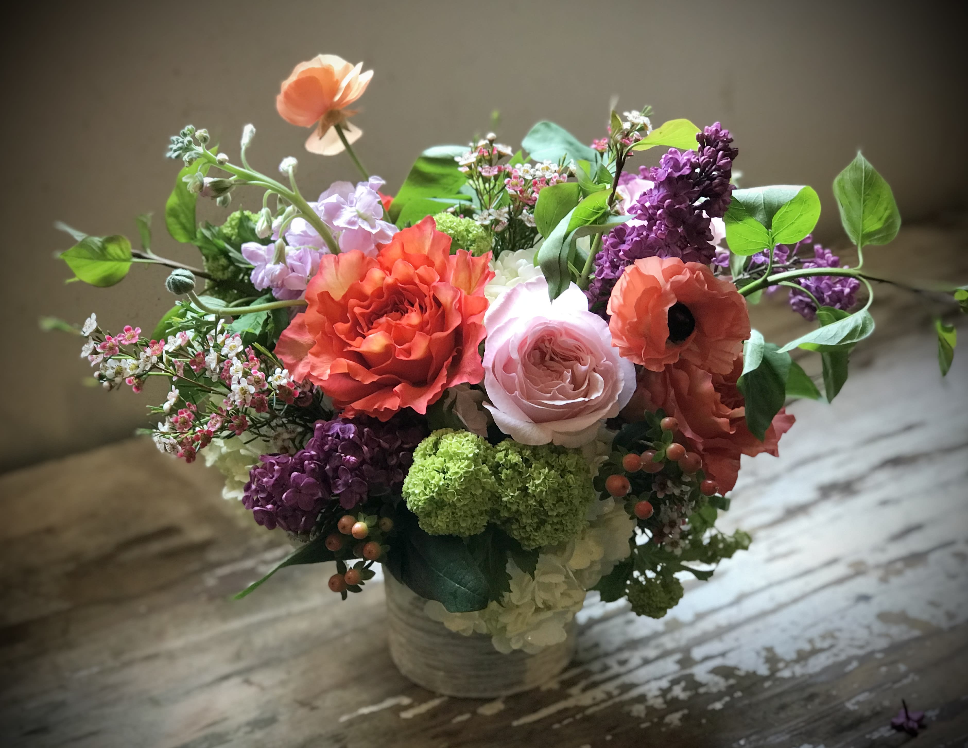 Mixed bouquet of coral, pink, purple, and white flowers in a low container