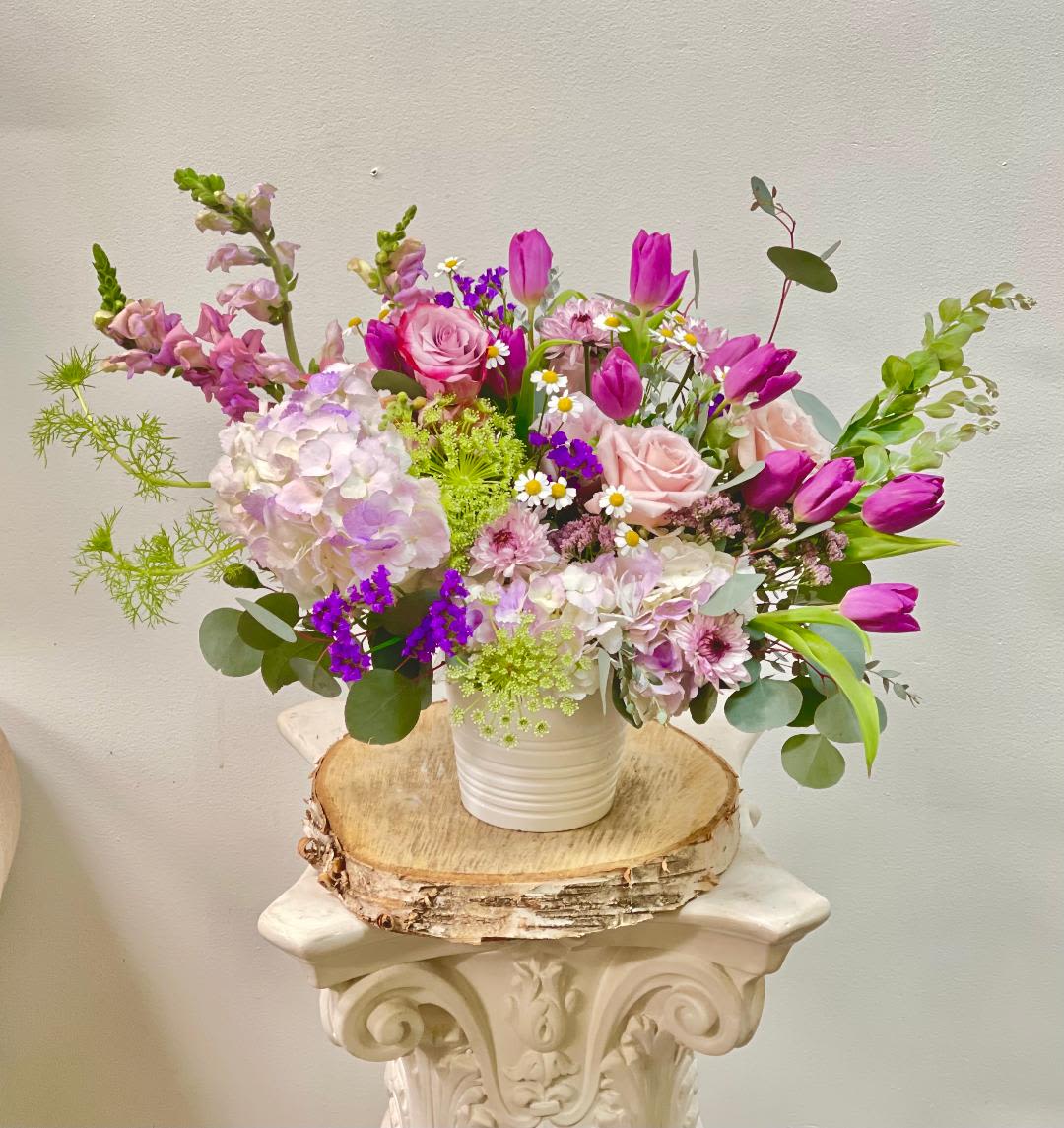 Mixed pink and purple flowers in a white vase on a wood slice