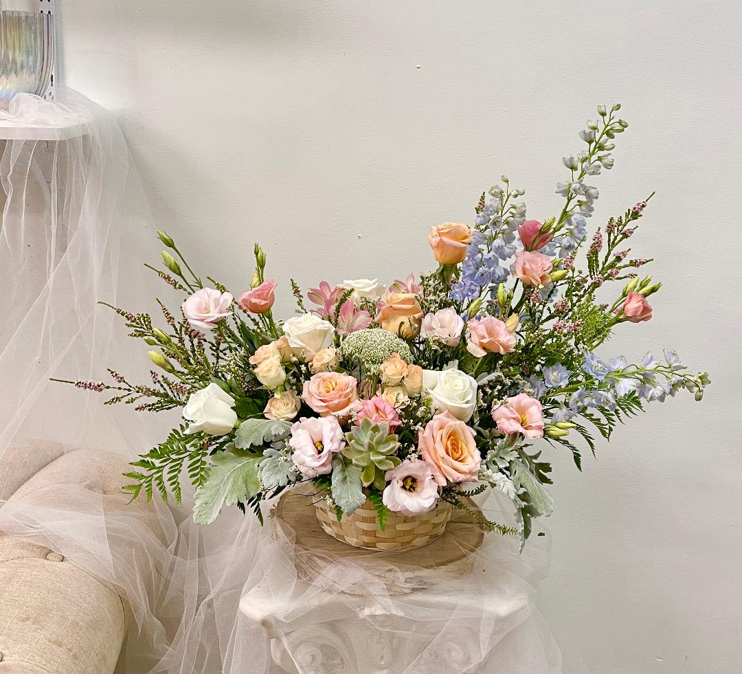Pastel bouquet of roses, lisianthus, and blue delphinium in a woven basket