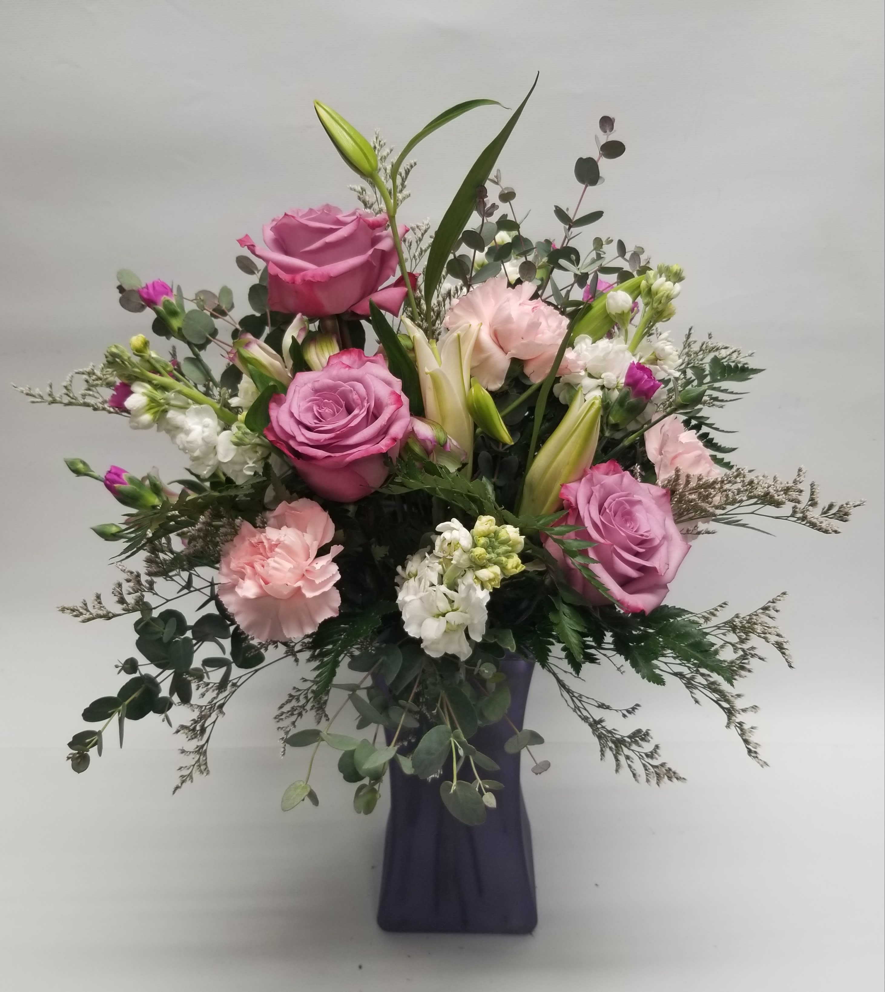Pink roses and lilies in a purple vase with greenery
