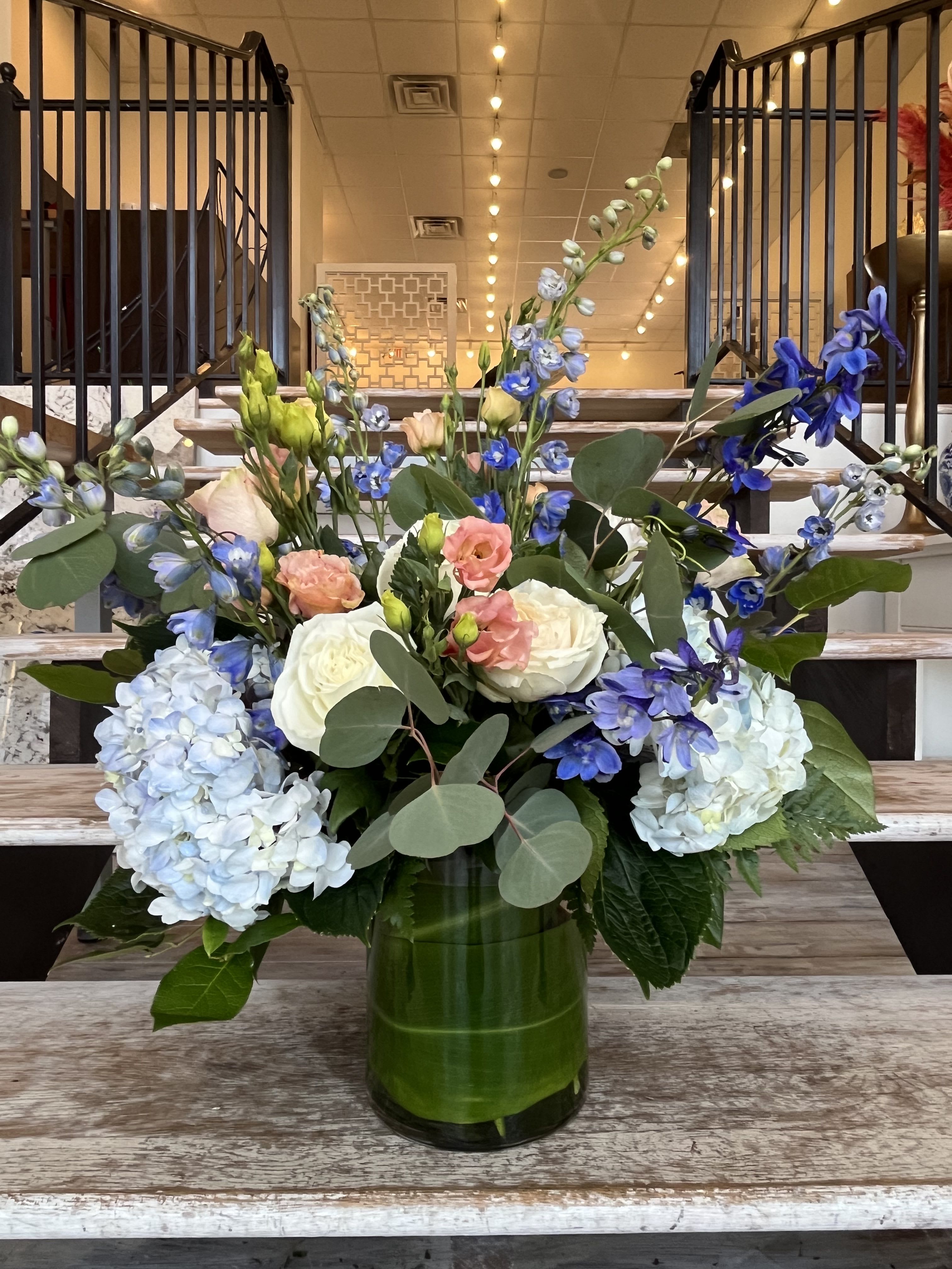 Mixed bouquet of blue and white flowers in a green glass vase