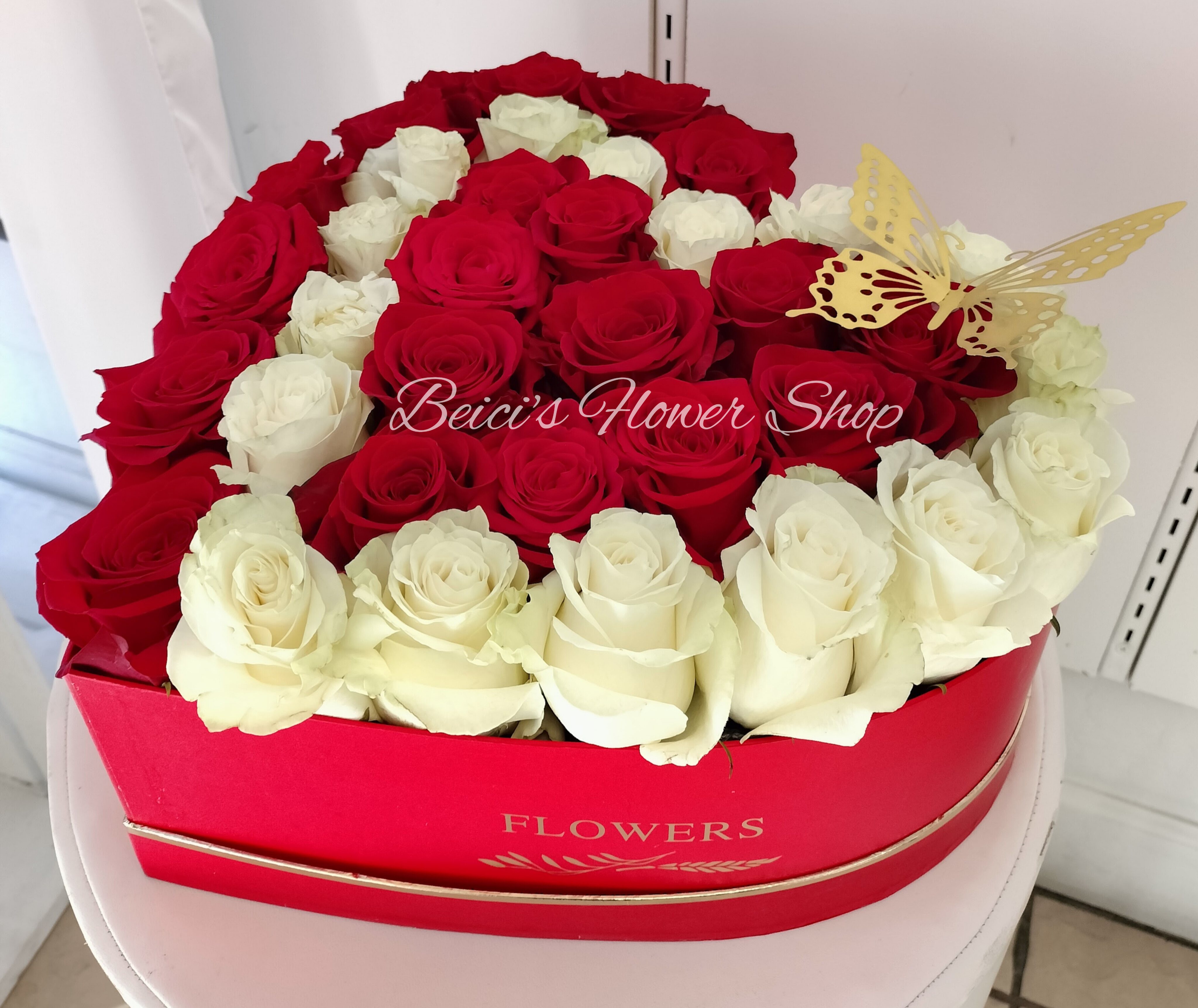 Red and white roses arranged in a heart-shaped box with a butterfly decoration