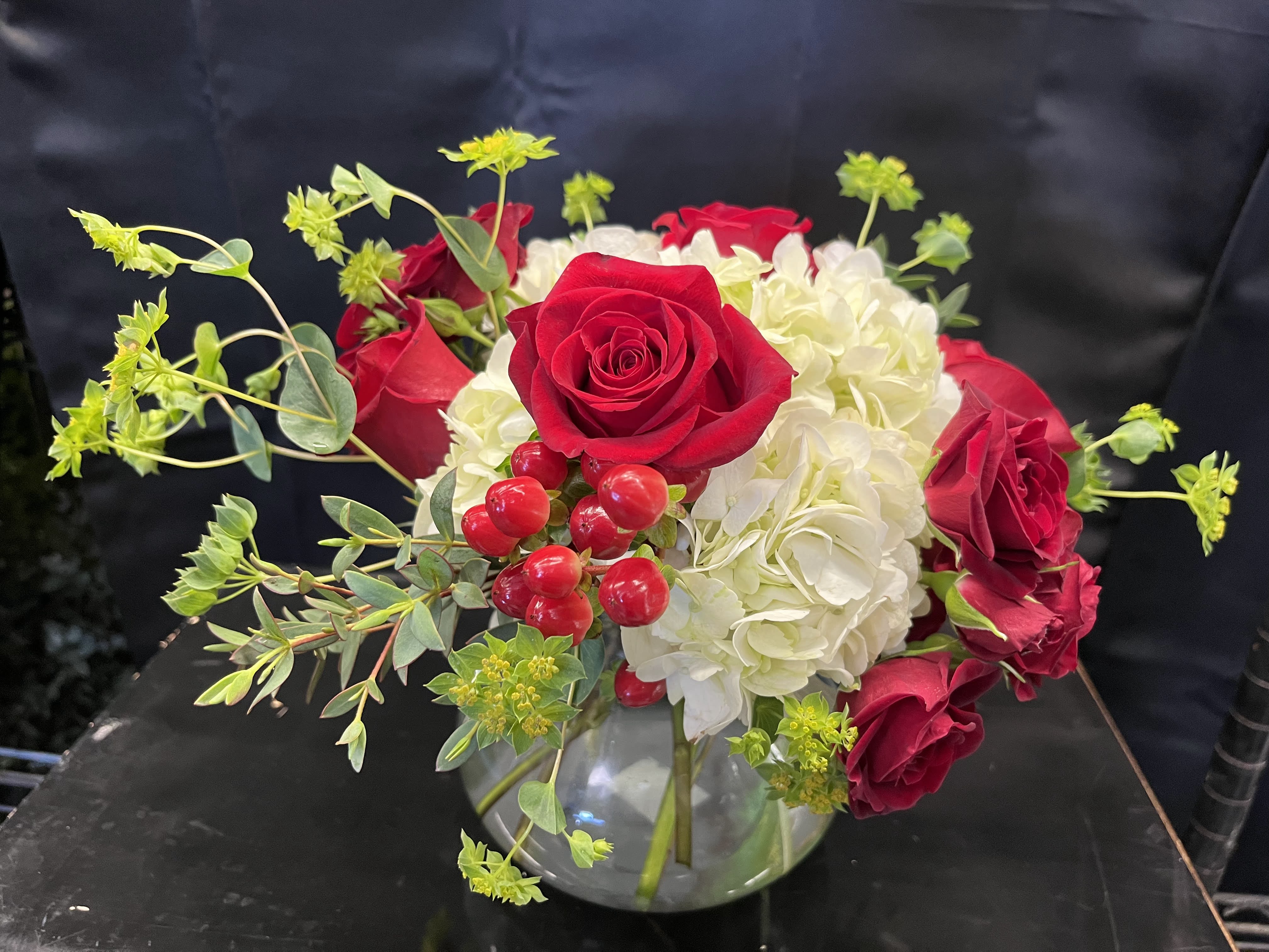 Red roses and white hydrangeas in a glass vase with red berries