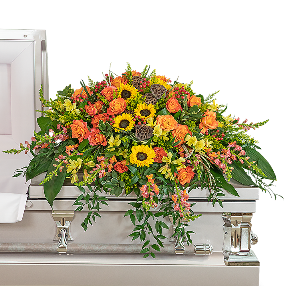 Sunset Reflections Casket Spray - The Sunset Reflections Casket Spray is brilliant and beautiful, featuring orange roses, snapdragons, hypericum berry, alstroemeria, bright sunflowers, solidago, and premium foliage. The casket spray is typically provided by the spouse or immediate family as a heartfelt memorial from the family and is designed to sit on the lid of the casket for a funeral service. Sunset Reflections is a radiant way to celebrate and reflect on an amazing life.   The image shows the Deluxe arrangement.