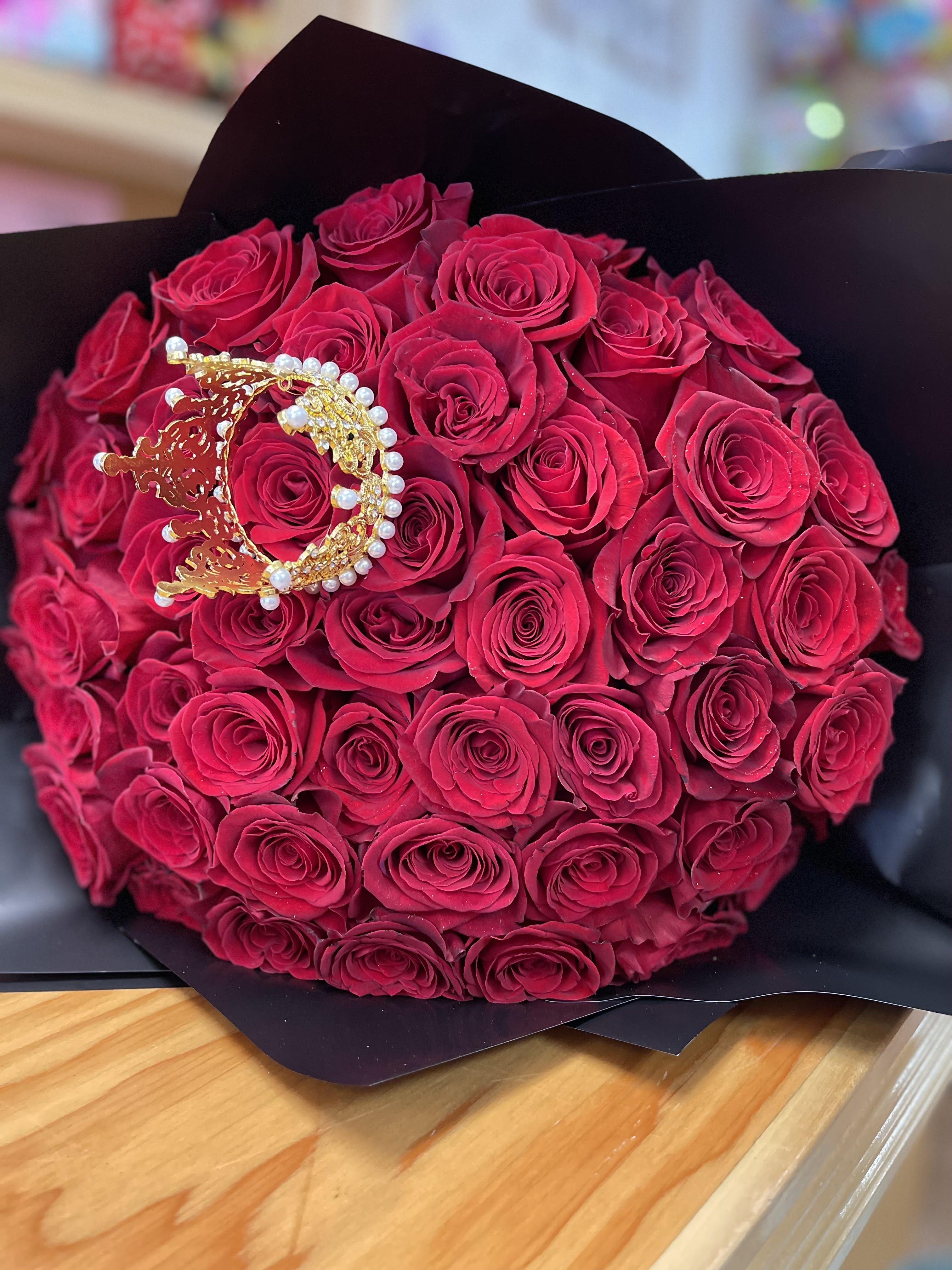 Bouquet of deep pink roses wrapped in black paper with a jeweled crown accent