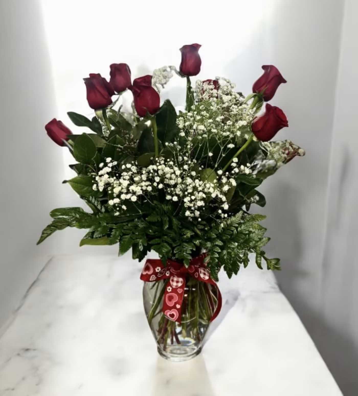 Red roses with baby's breath in a glass vase with a heart ribbon