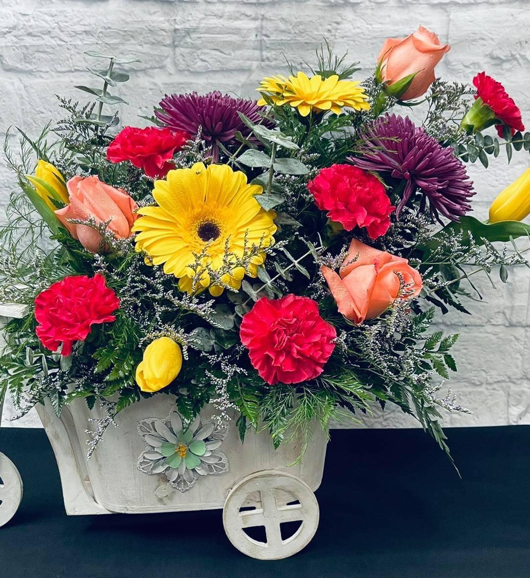 Mixed bouquet in a white decorative cart with yellow, pink, and peach blooms