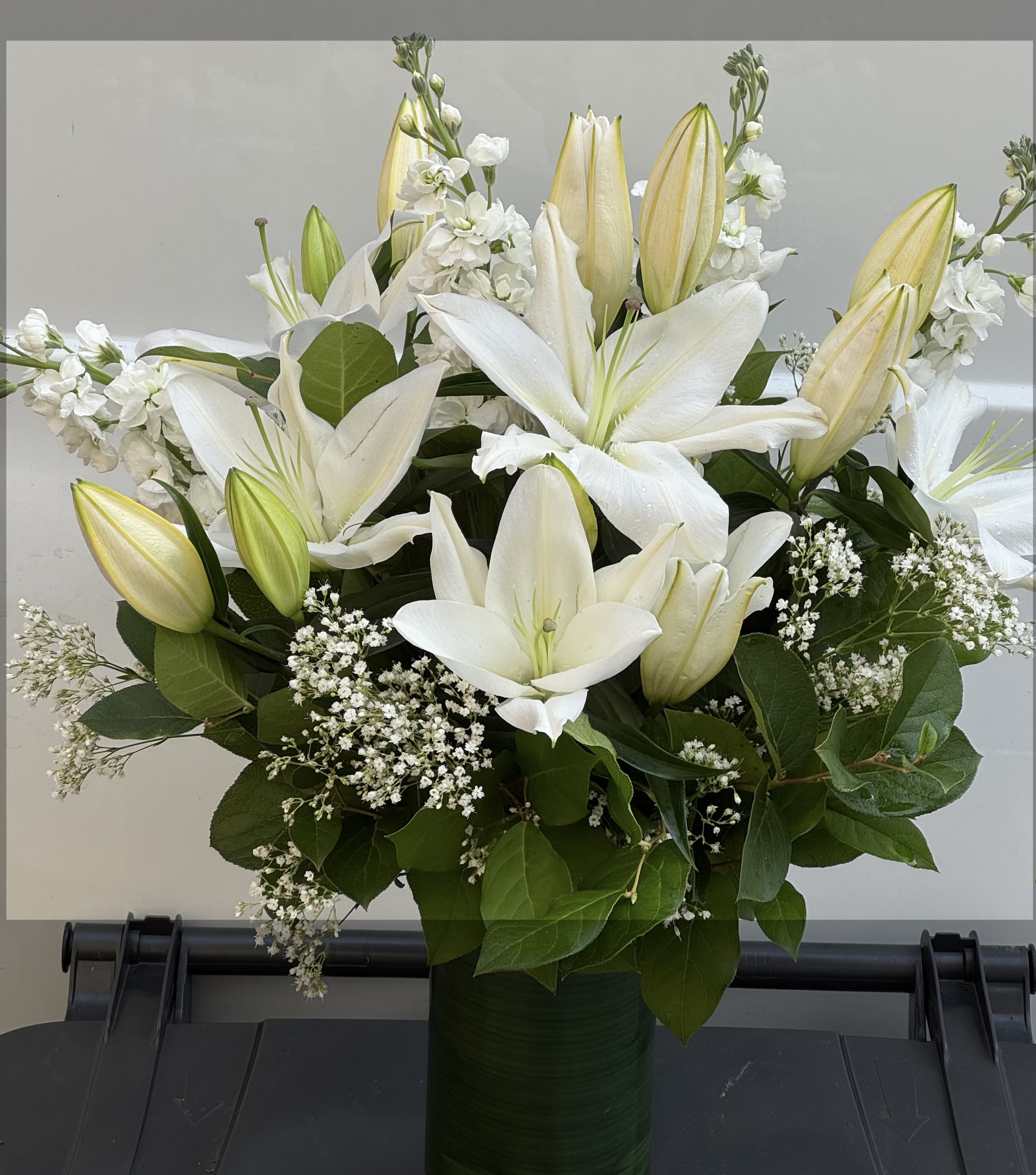 White lilies and buds arranged in a green vase with baby's breath