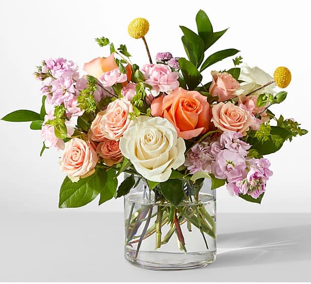 Peach, pink, and white roses with accent flowers arranged in a clear glass vase