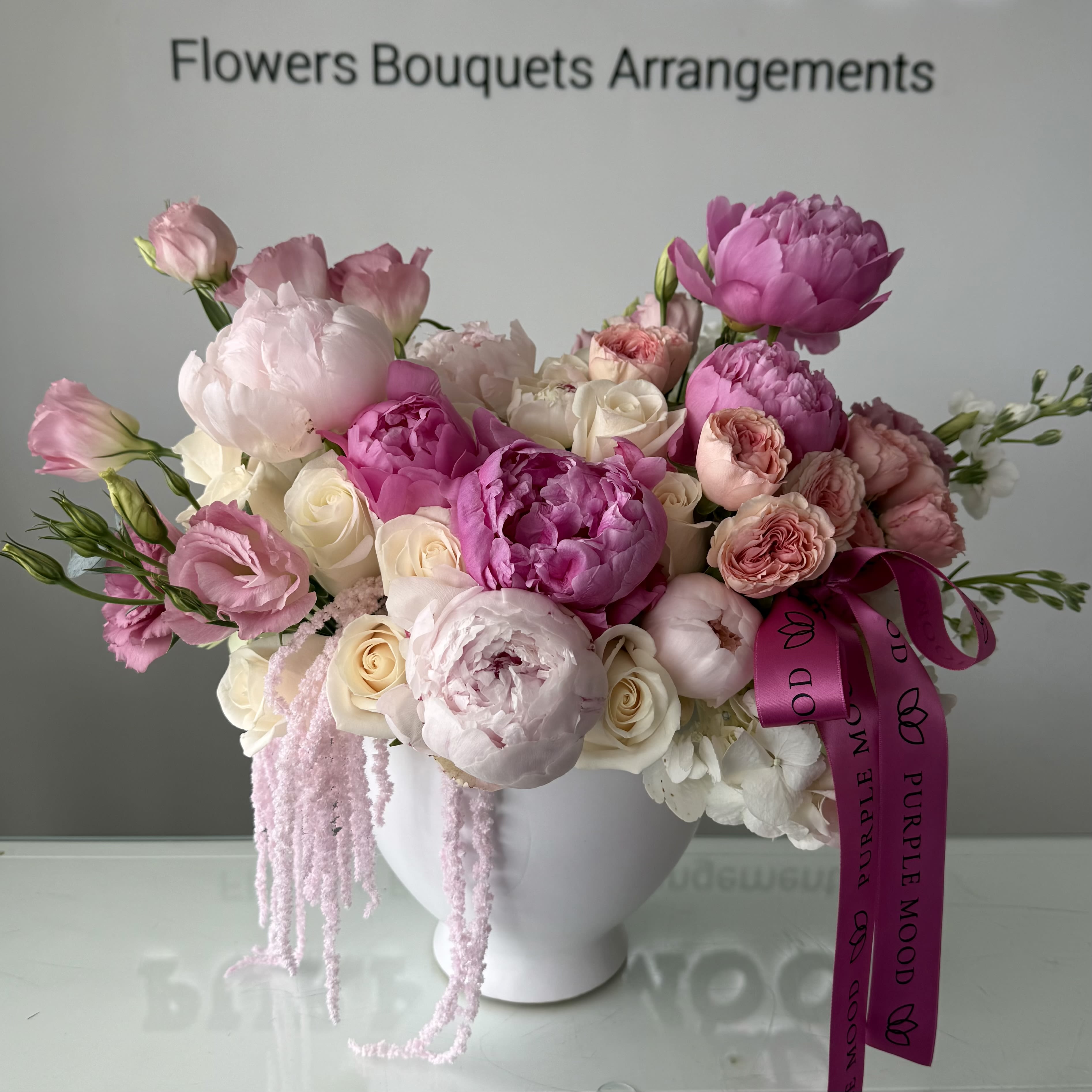 Queen Vase - A soft, romantic arrangement in delicate shades of blush and cream, designed to feel light, airy, and elegant. Featuring lush peonies, garden roses, and lisianthus, this piece brings a refined, feminine touch to any space. Arranged in a modern white vase and finished with our signature ribbon, it’s perfect for celebrations, gifts, or simply elevating everyday moments. 