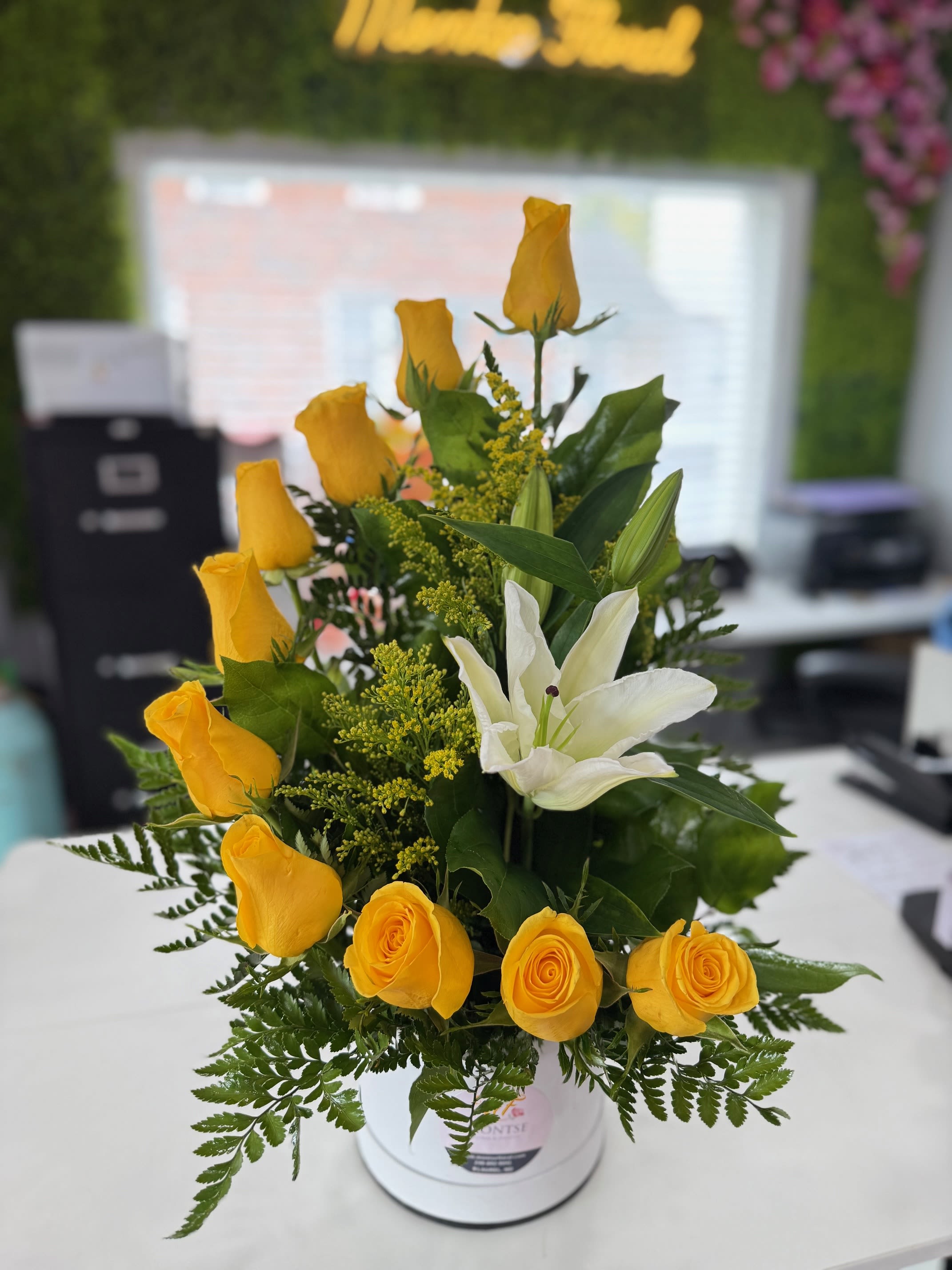 Yellow roses and a white lily arranged in a white vase